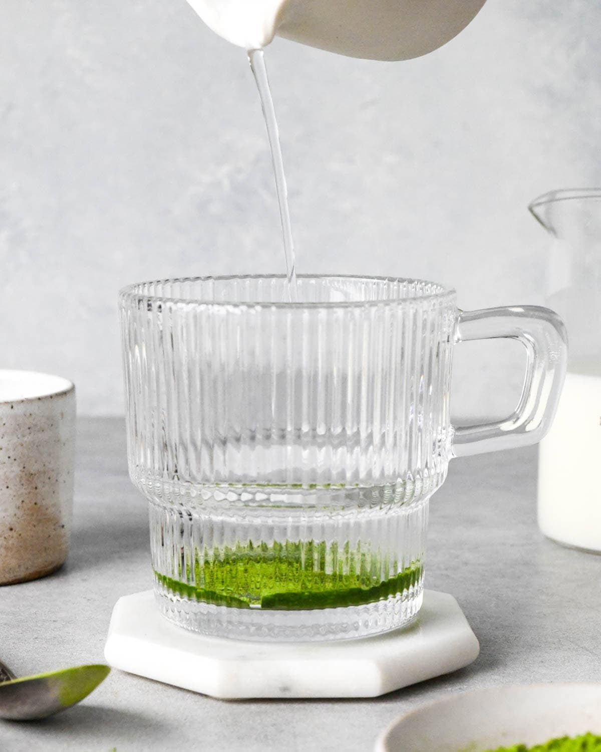 photo showing how to make a matcha latte - front view of hot water being poured into matcha powder in a glass mug