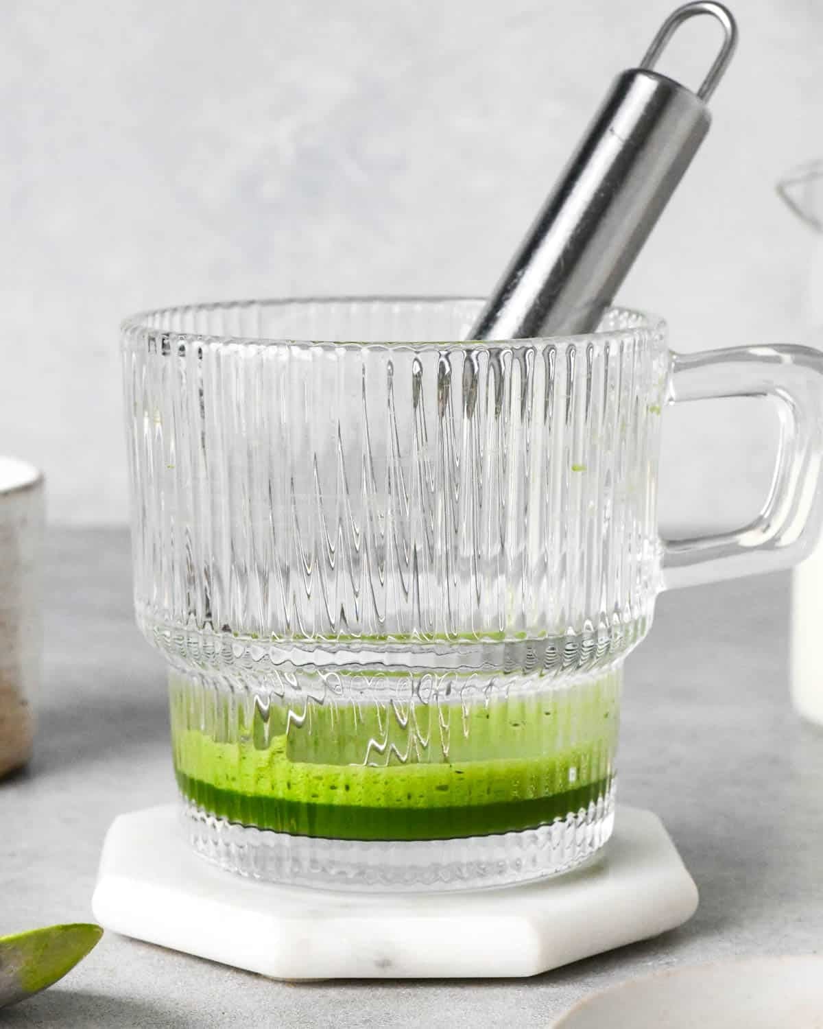 photo showing how to make a matcha latte - front view of hot water and matcha powder being whisked together in a glass mug
