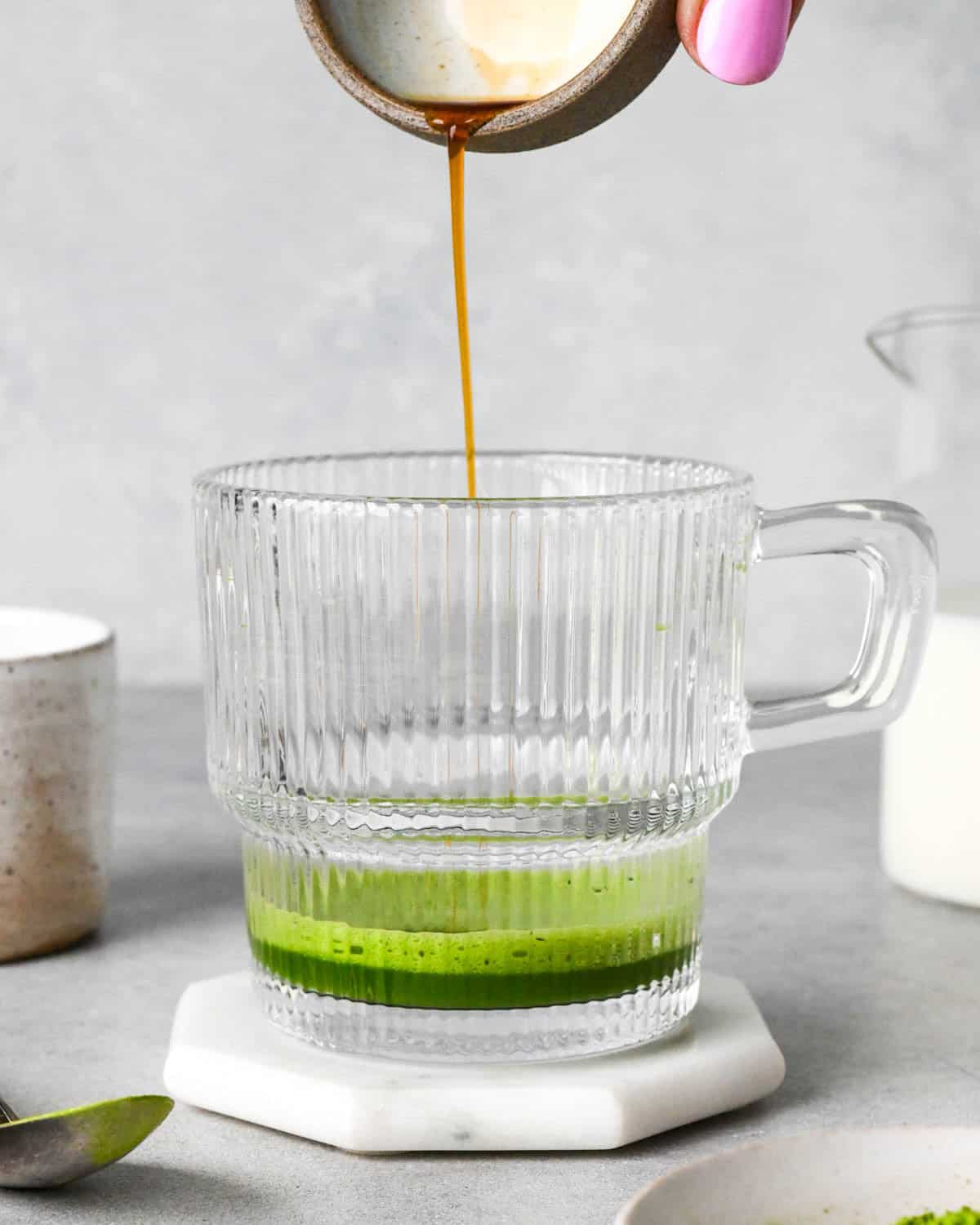 photo showing how to make a matcha latte - front view of vanilla being poured into a glass mug with matcha powder and hot water