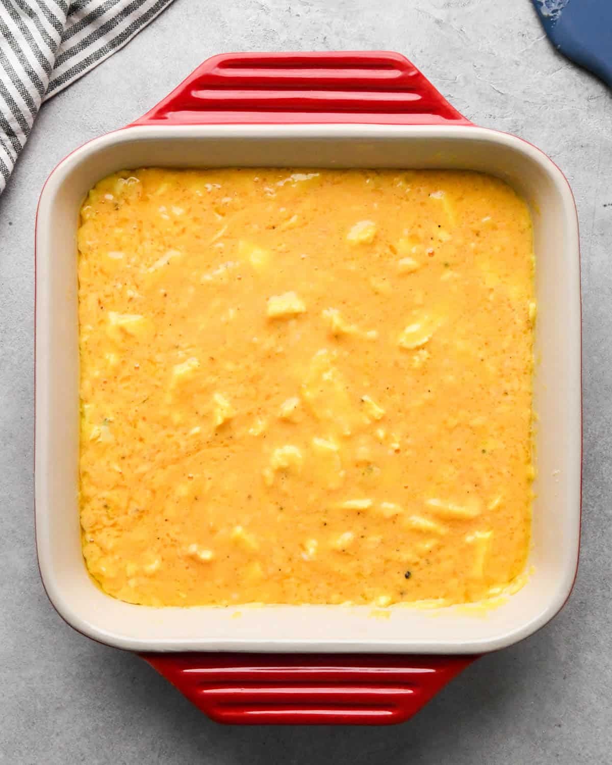 photo showing how to make baked scrambled eggs - partially baked egg mixture in a red, square, ceramic baking dish