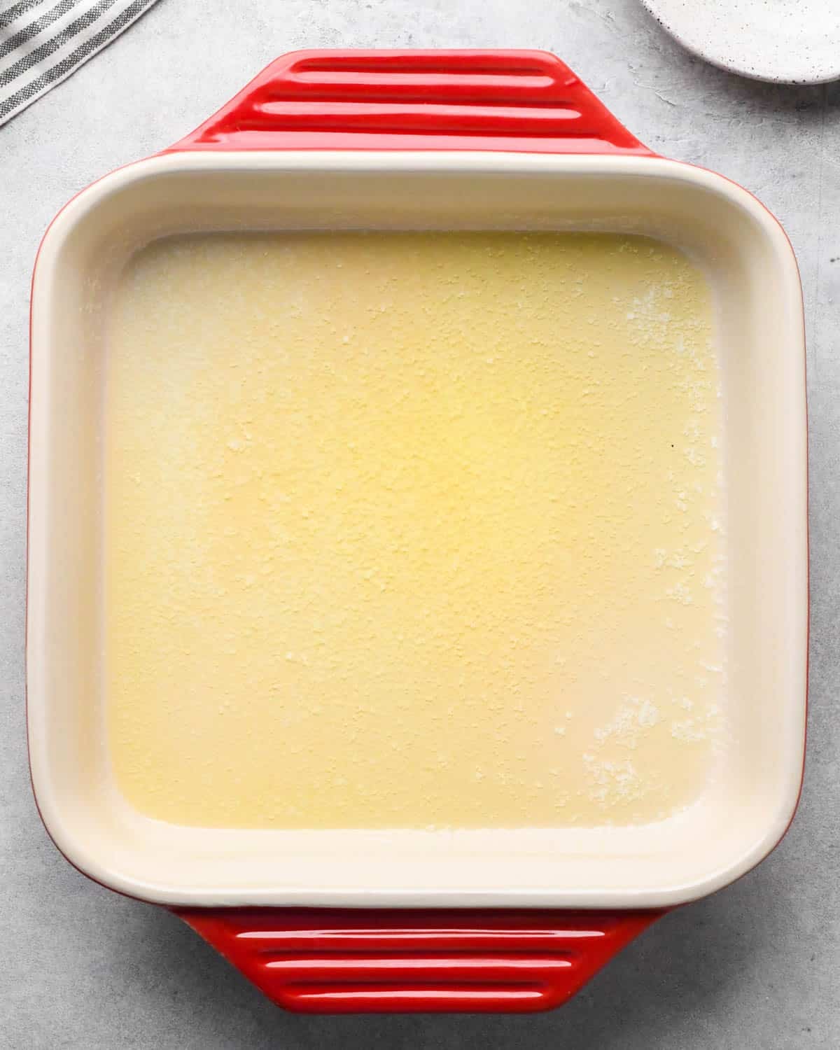 photo showing how to make baked scrambled eggs - melted butter in a red ceramic square baking dish