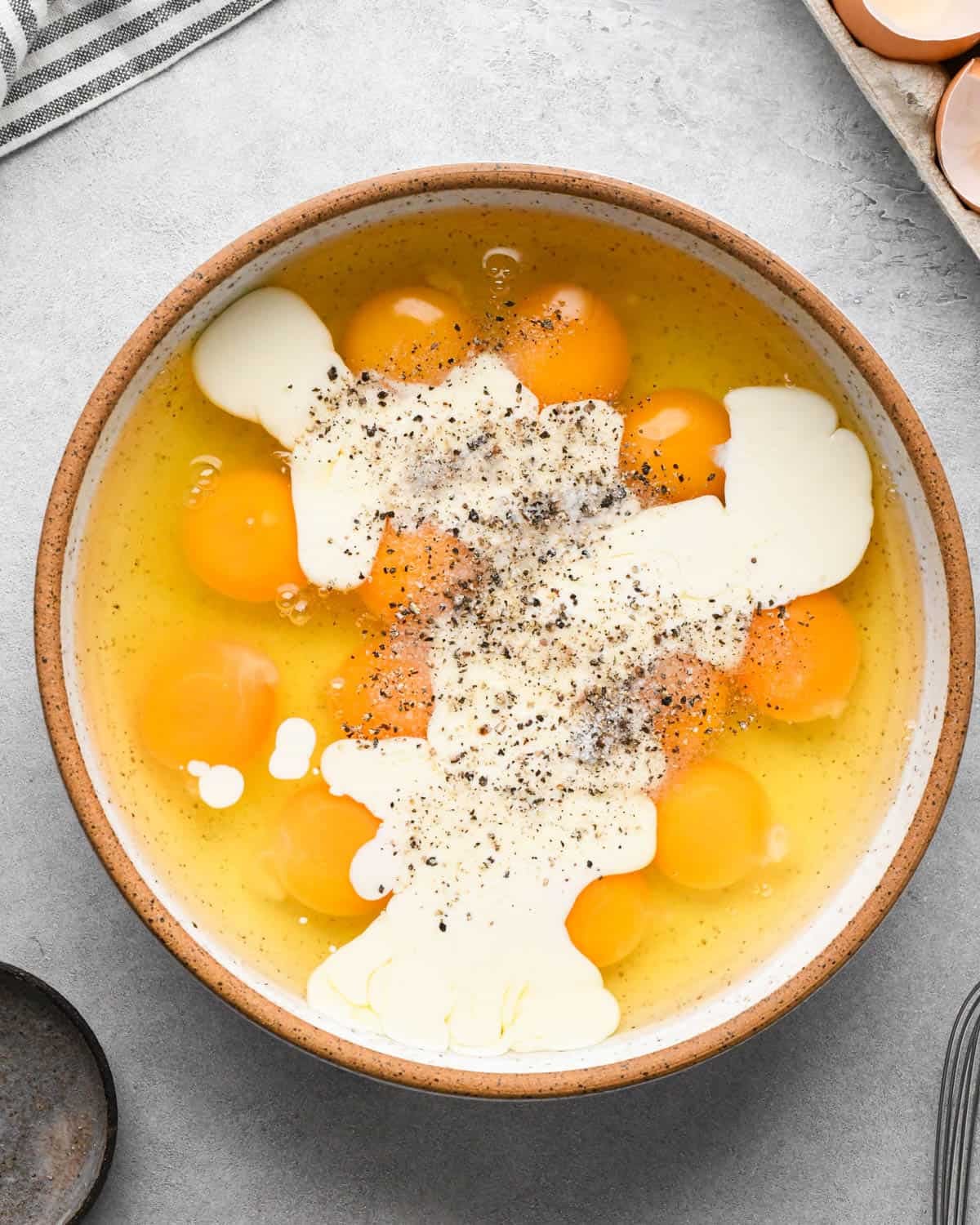 photo showing how to make baked scrambled eggs - eggs, cream, salt and pepper in a large ceramic mixing bowl before whisking