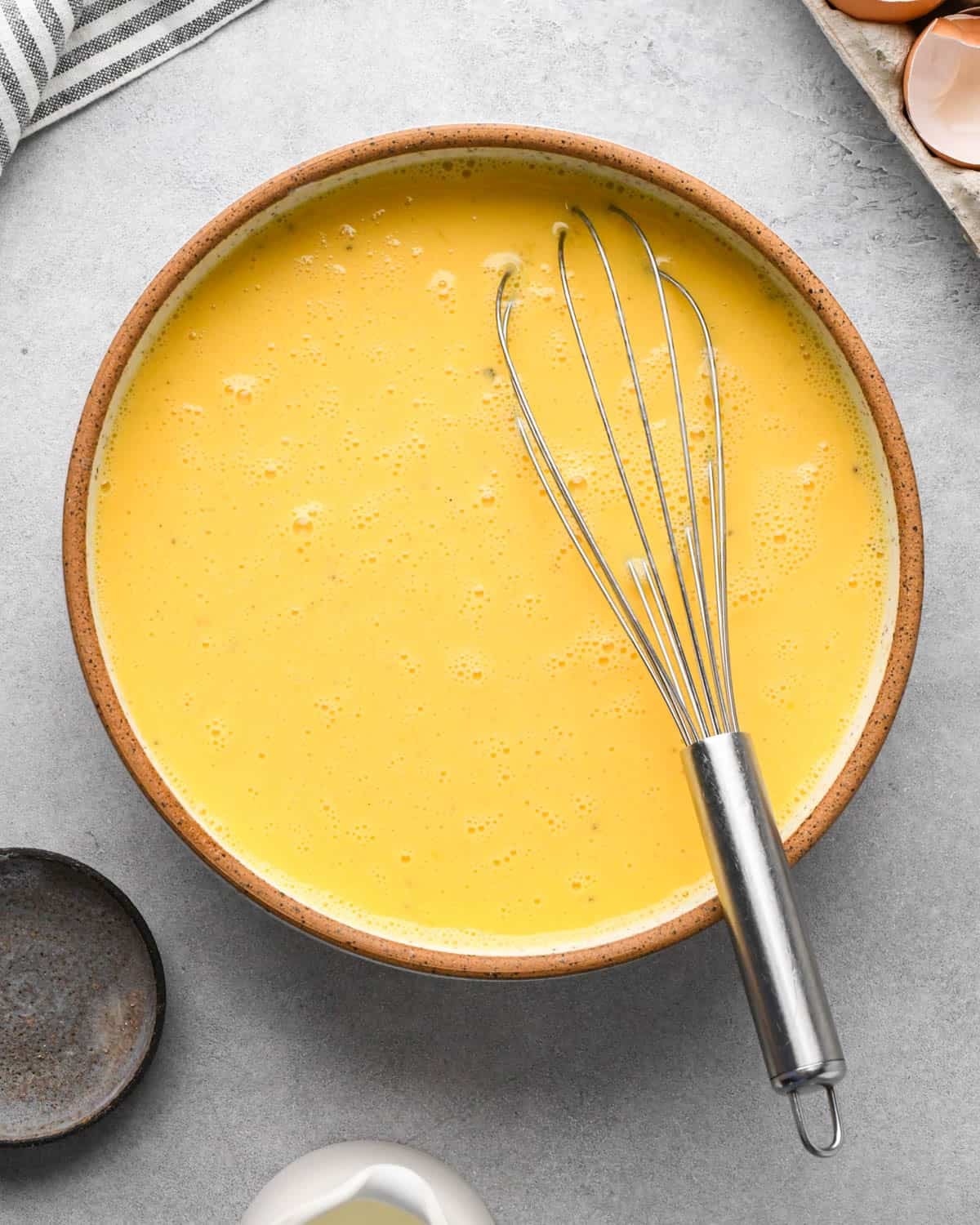 photo showing how to make baked scrambled eggs - eggs, cream, salt and pepper in a large ceramic mixing bowl after whisking