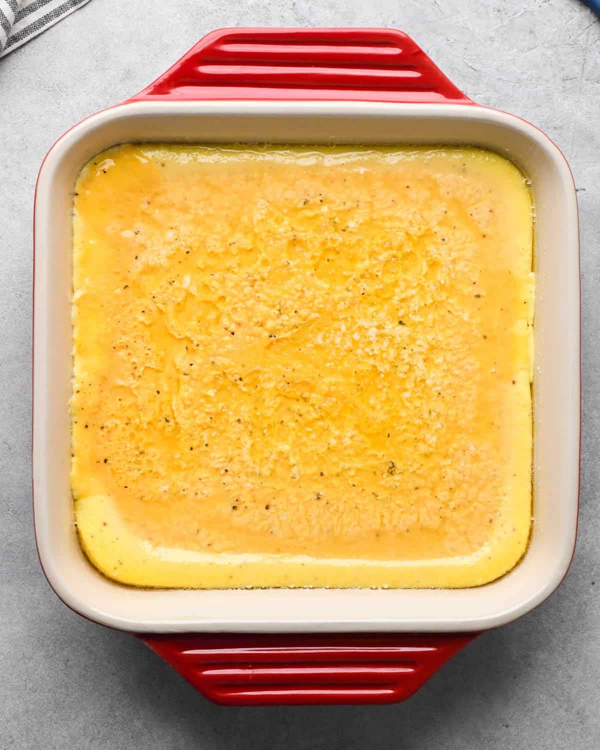 photo showing how to make baked scrambled eggs - egg mixture in a red, square, ceramic baking dish after they have been partially baked