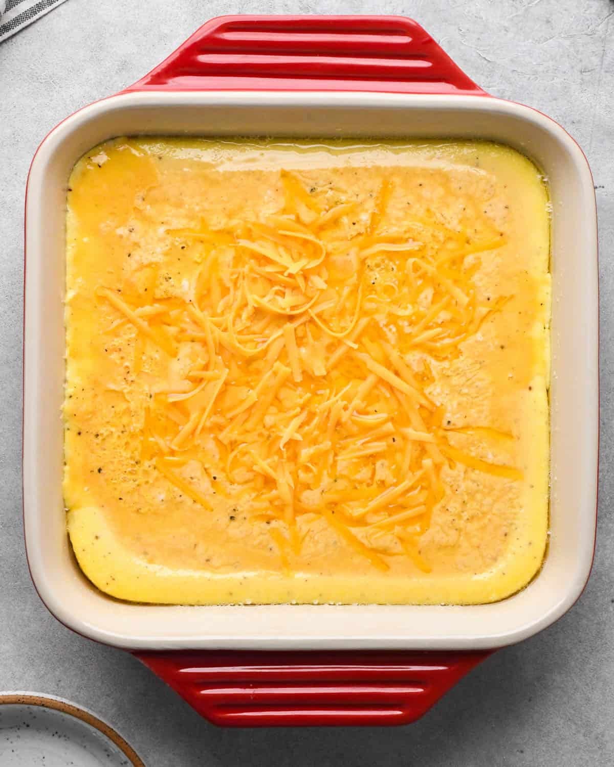 photo showing how to make baked scrambled eggs - cheese added to the egg mixture in a red, square, ceramic baking dish after it has been partially baked before stirring in the cheese