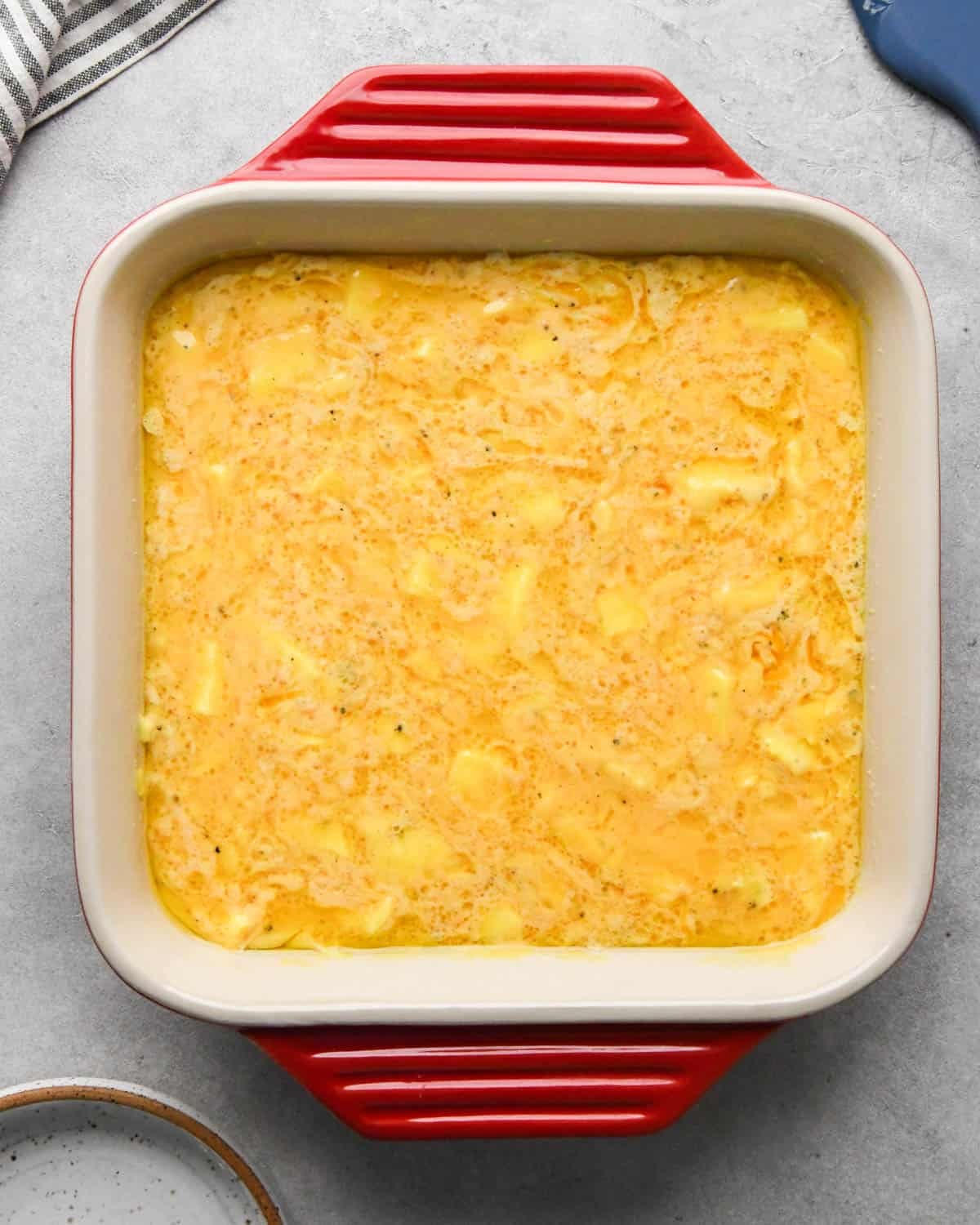 photo showing how to make baked scrambled eggs - partially baked egg mixture in a red, square, ceramic baking dish