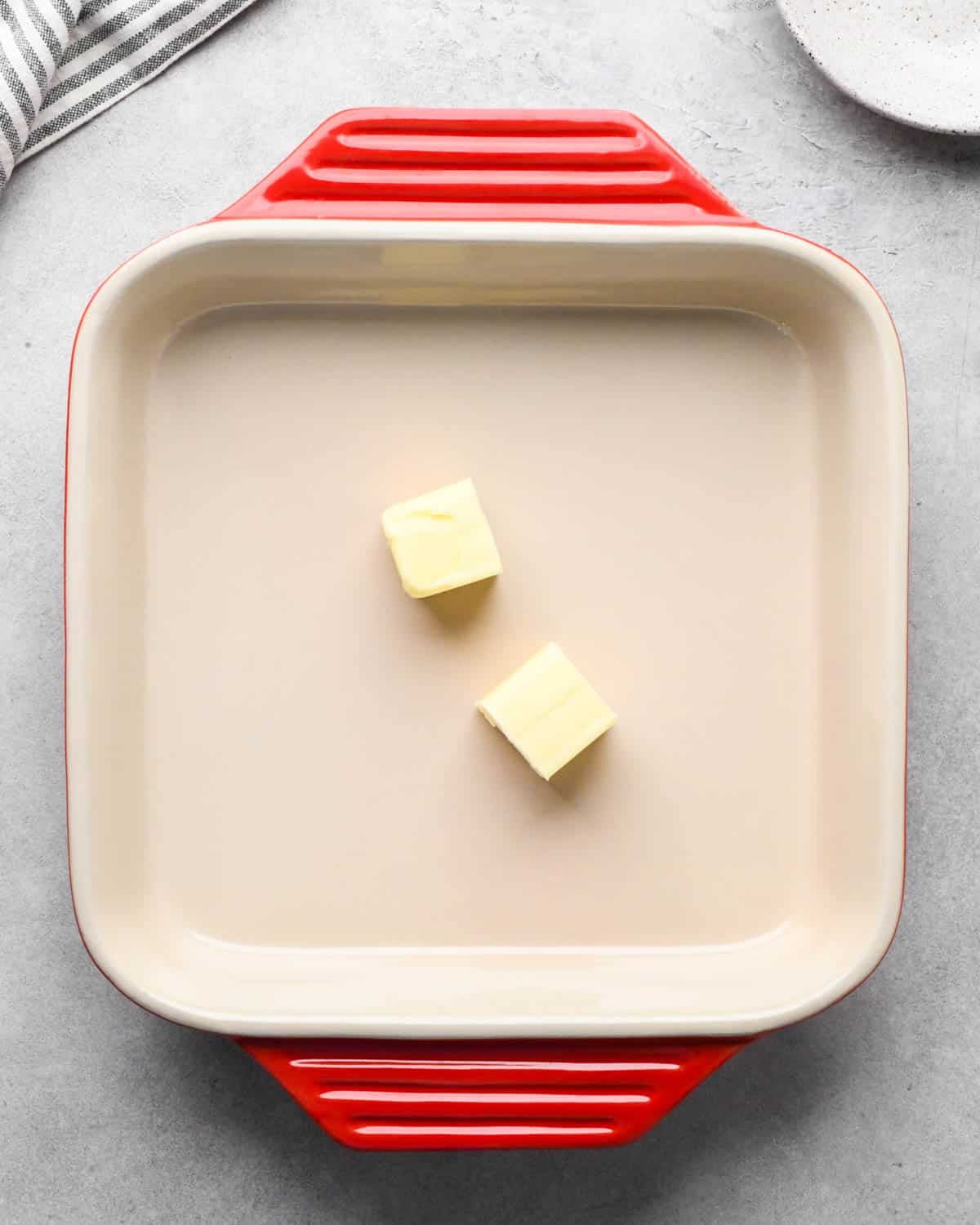 photo showing how to make baked scrambled eggs - two squares of butter in a red ceramic square baking dish
