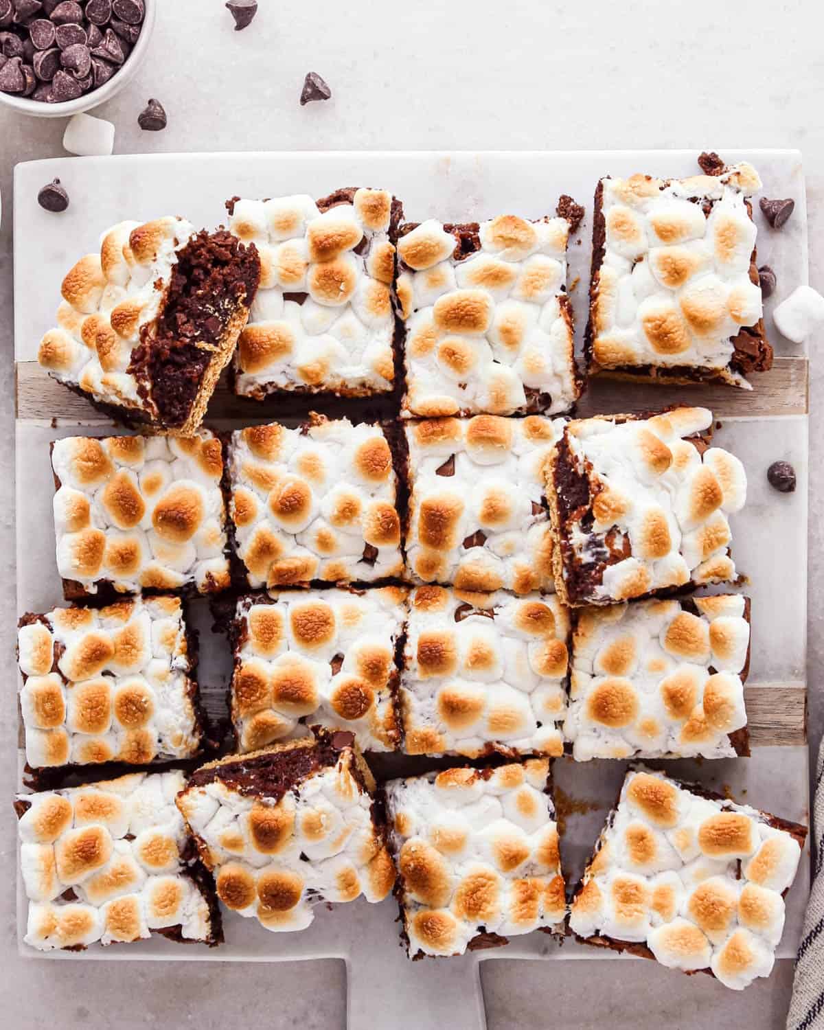 16 s'mores brownies cut into squares on a cutting board with a graham cracker crust and toasty marshmallow top