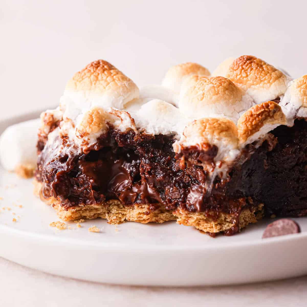 a s'mores brownie with a bite taken out of it on a plate. It has a graham cracker crust and toasted marshmallow top
