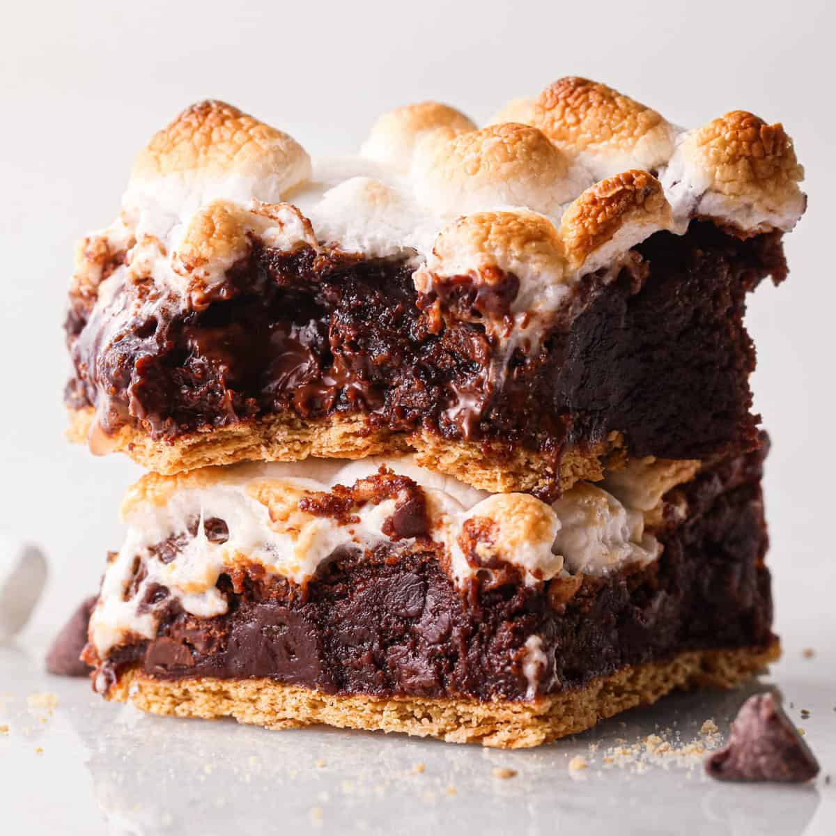 a stack of two s'mores brownies with a graham cracker crust on bottom and toasted marshmallows on top. The top brownie has a bite taken out of it so the fudgy texture of the brownie is visible.