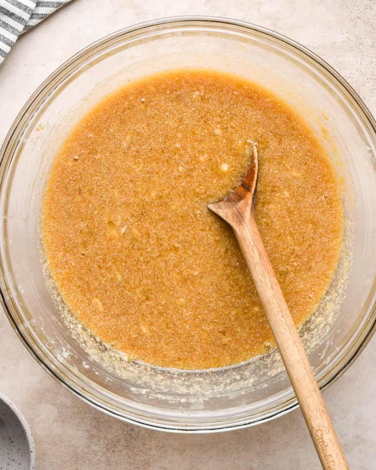 making brown butter banana bread - wet ingredient and sugar mixture in a glass bowl with a wooden spoon