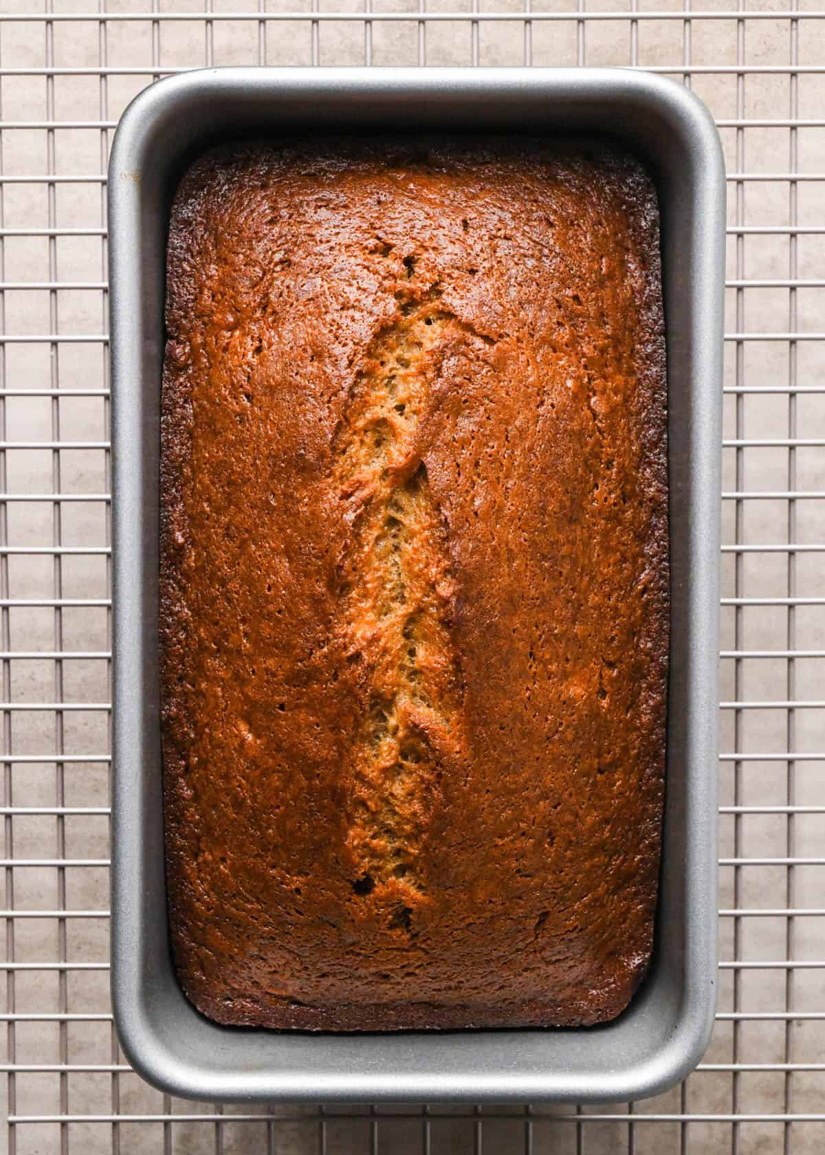 baked brown butter banana bread in a metal loaf pan on a metal cooling rack