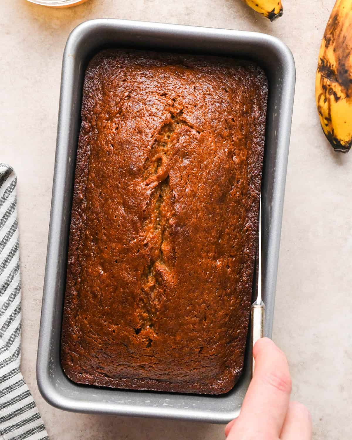 a knife releasing the edges of brown butter banana bread in a metal loaf pan