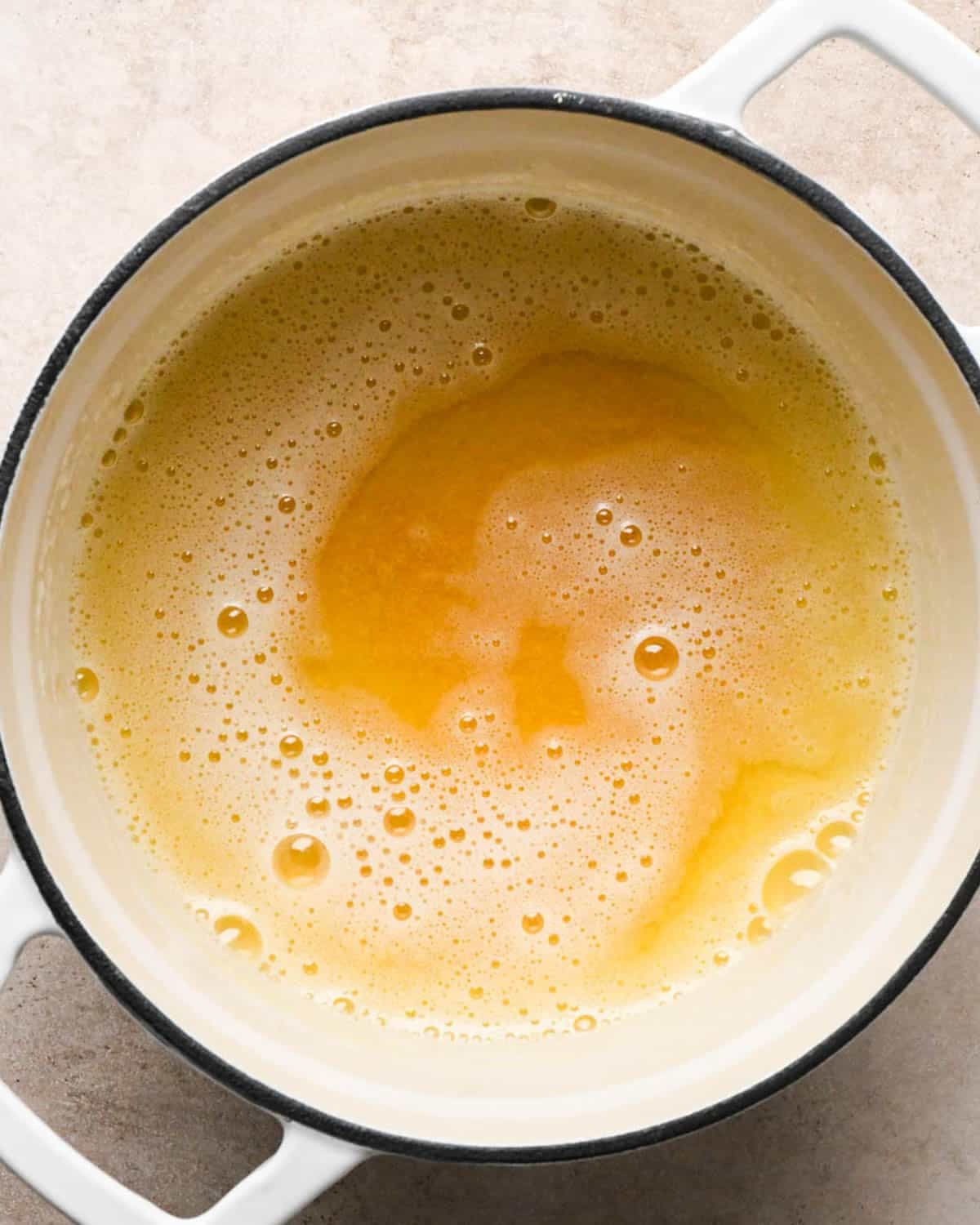 browning the butter for brown butter banana bread in a white pot - butter is melted, starting to foam and turn darker