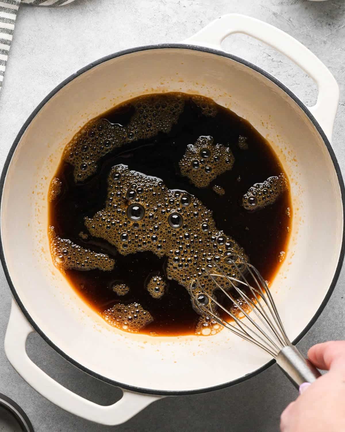 making teriyaki sauce for teriyaki meatballs - ingredients being whisked with a metal whisk in a white saucepan with a black rim