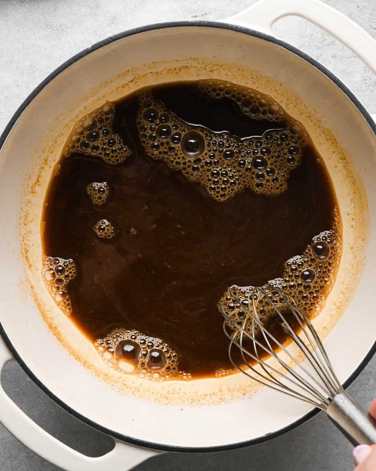making teriyaki sauce for teriyaki meatballs - ingredients being whisked with a metal whisk in a white saucepan with a black rim