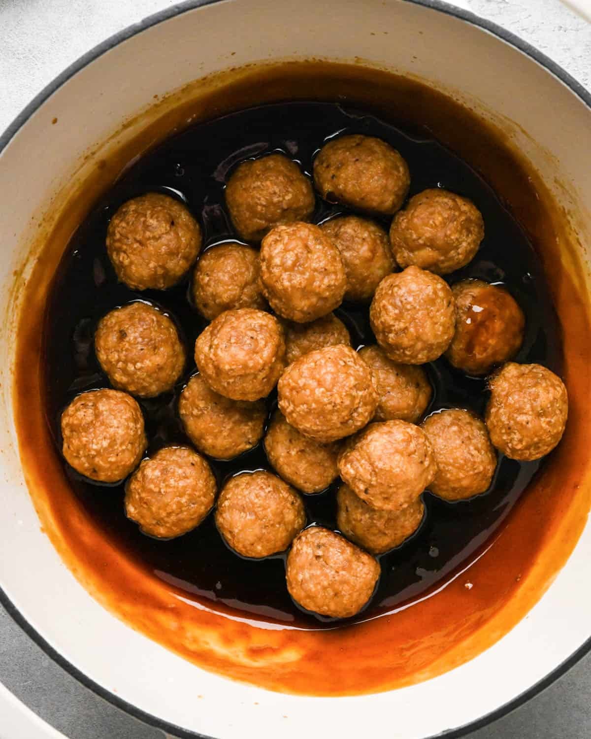 teriyaki meatballs in a white saucepan with a black rim coated in teriyaki sauce