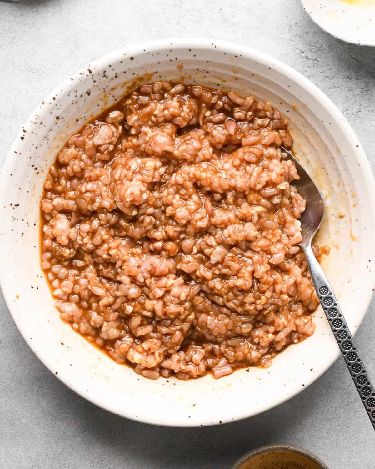 making teriyaki meatballs - ground chicken, egg, soy sauce, hoisin sauce, and sesame oil in a ceramic mixing bowl with a metal spoon after mixing