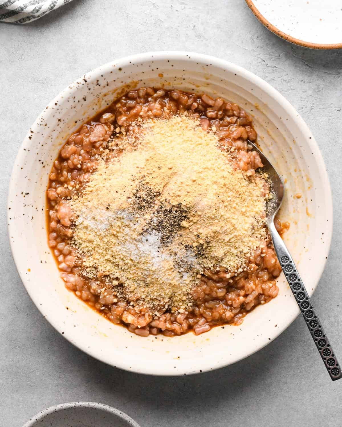 making teriyaki meatballs - dry ingredients including bread crumbs and seasonings added to the wet mixture in a ceramic mixing bowl with a metal spoon before mixing