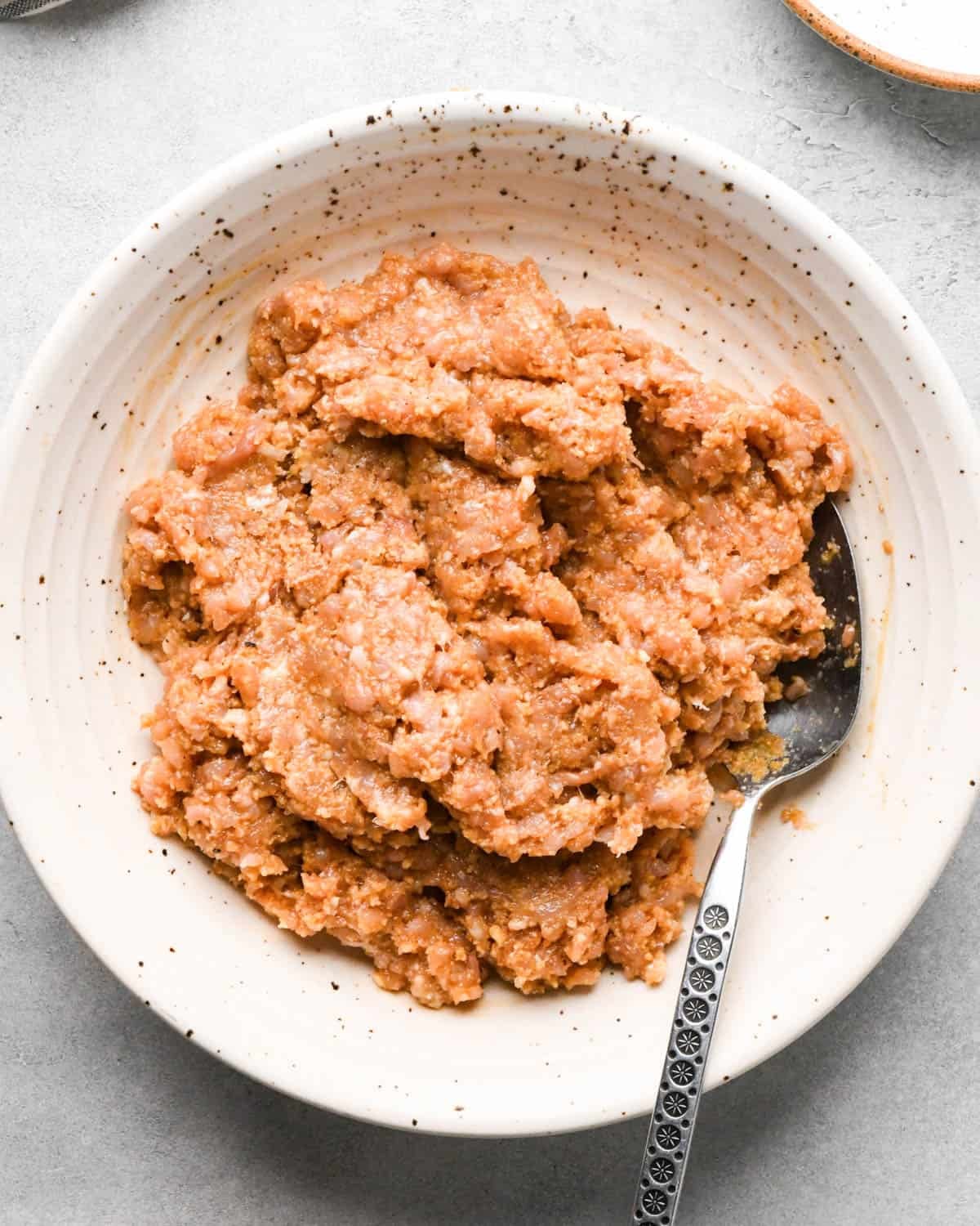 final teriyaki chicken meatballs mixture in a ceramic bowl with a metal spoon