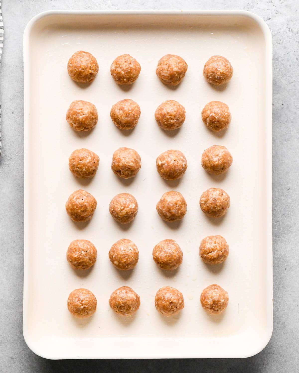 24 teriyaki chicken meatballs on a white baking sheet before baking