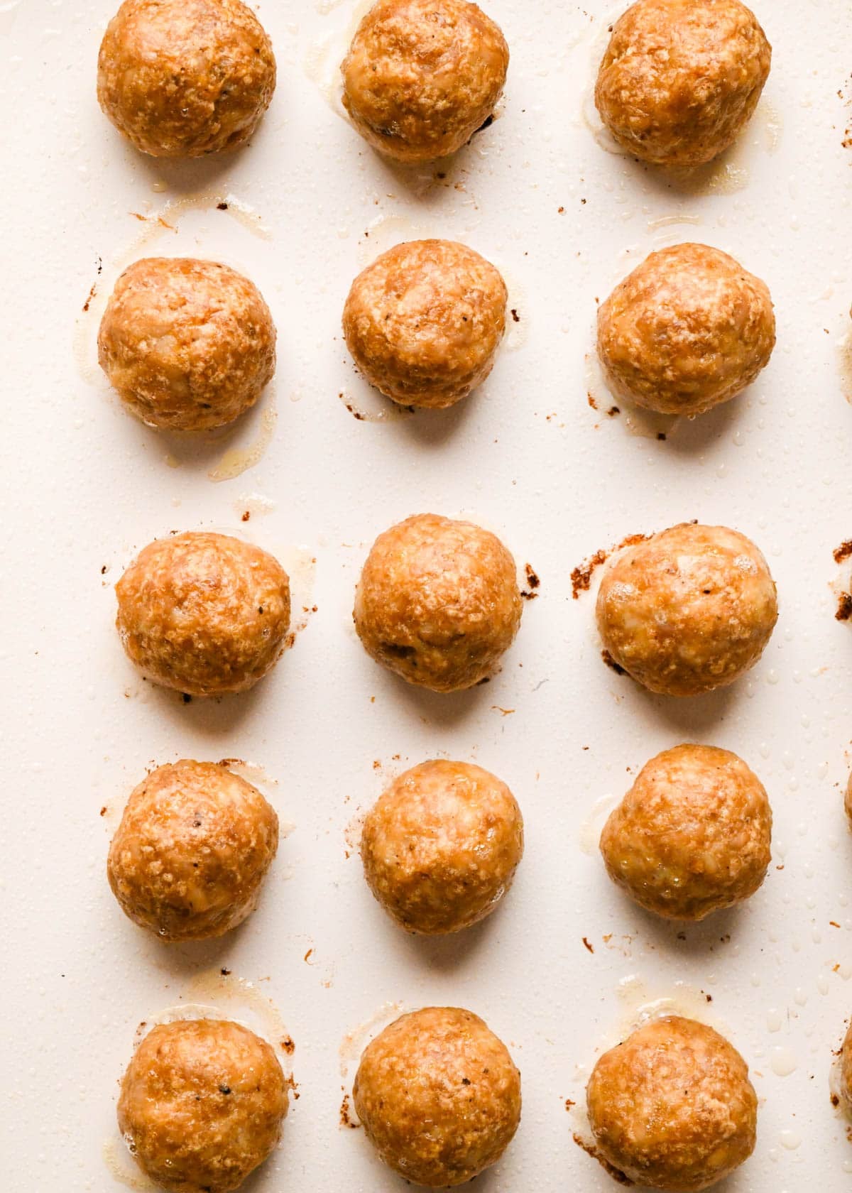 close up photo of 15 baked teriyaki meatballs on a baking sheet