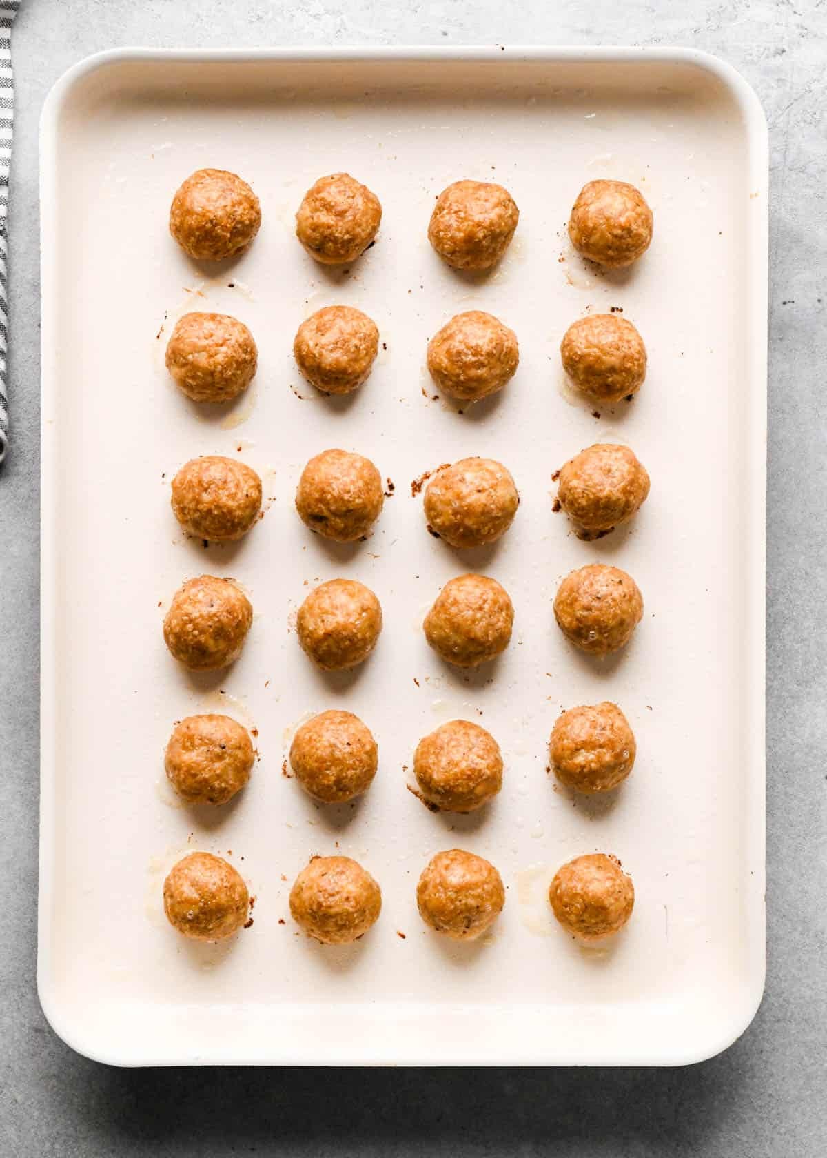 24 teriyaki chicken meatballs on a white baking sheet after baking