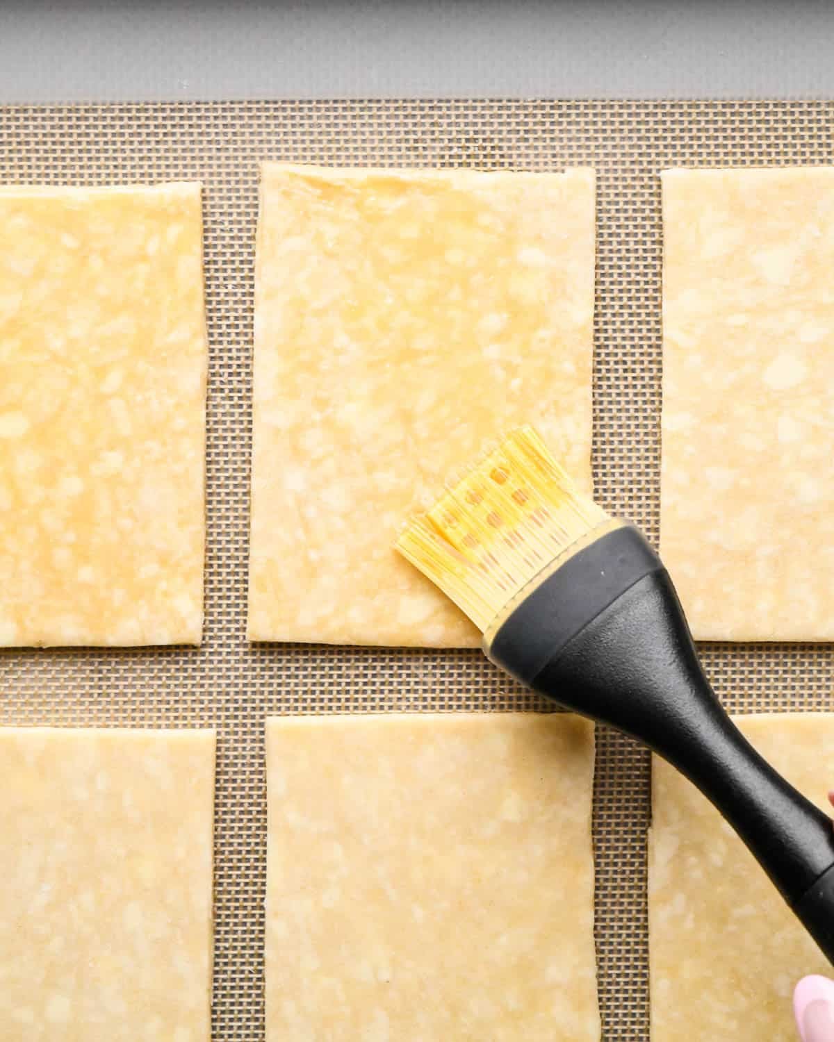 making homemade pop tarts - egg wash being brushed onto a rectangle of pastry dough