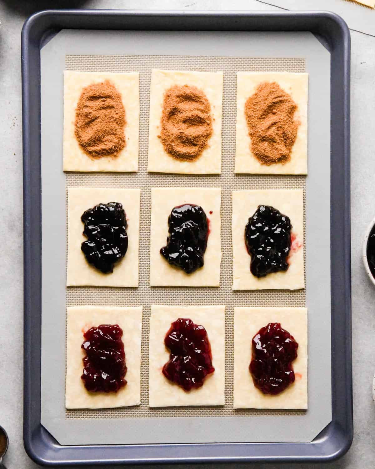 making homemade pop tarts - 9 rectangles of dough, 3 with strawberry jam, 3 with blackberry jam and 3 with cinnamon sugar on a baking sheet