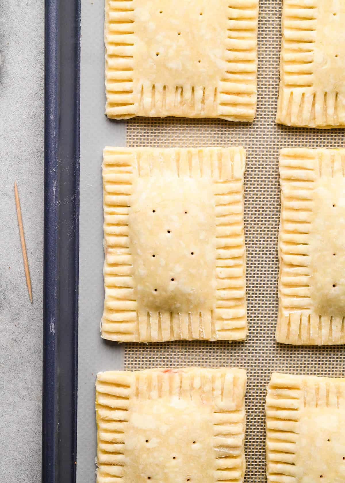 making homemade pop tarts - 6 pop tarts with holes punched into the top on a baking sheet lined with a silicone baking mat before baking