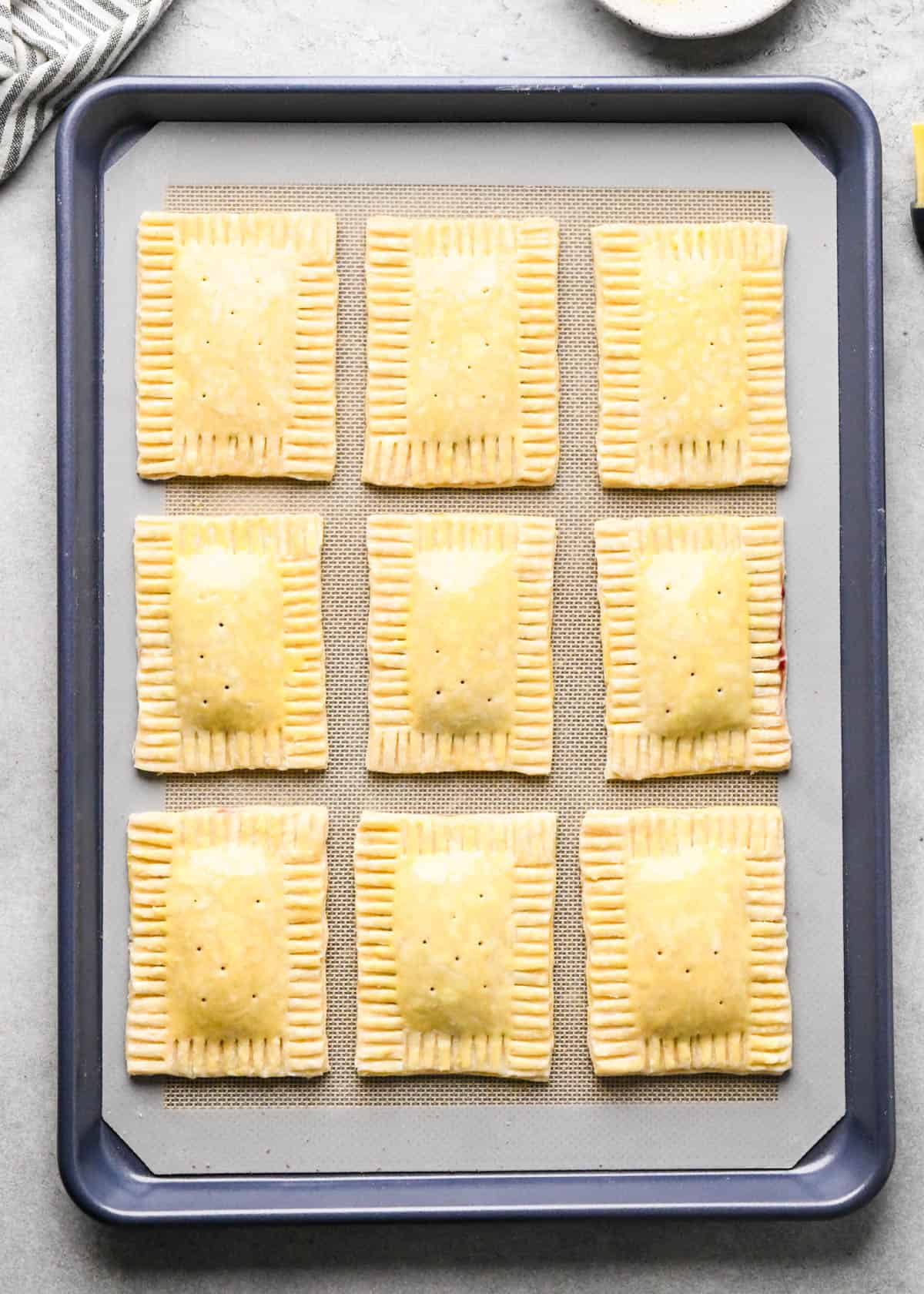 making homemade pop tarts - 9 pop tarts on a baking sheet lined with a silicone baking mat before baking