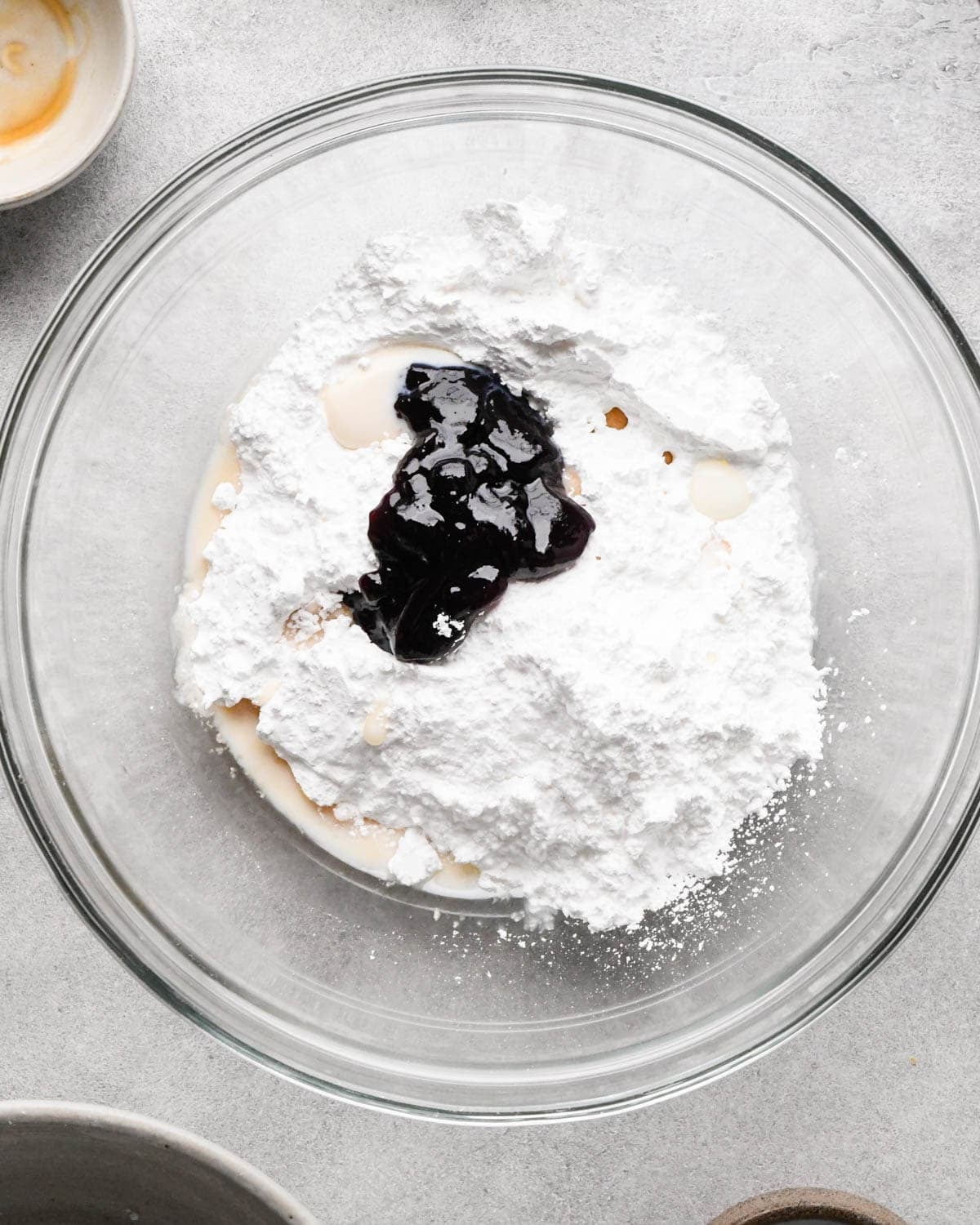 making icing for homemade pop tarts - blackberry jam, powdered sugar, milk and vanilla in a glass bowl before mixing
