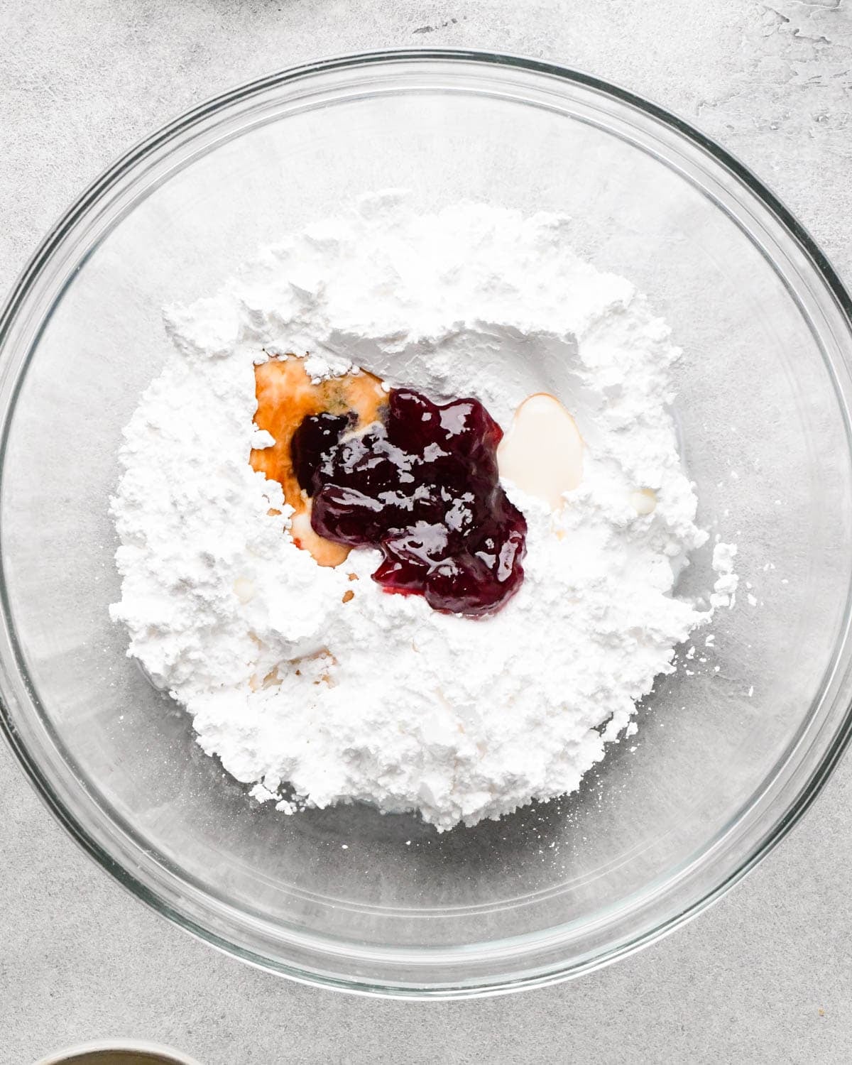 making icing for homemade pop tarts - strawberry jam, powdered sugar, milk and vanilla in a glass bowl before mixing