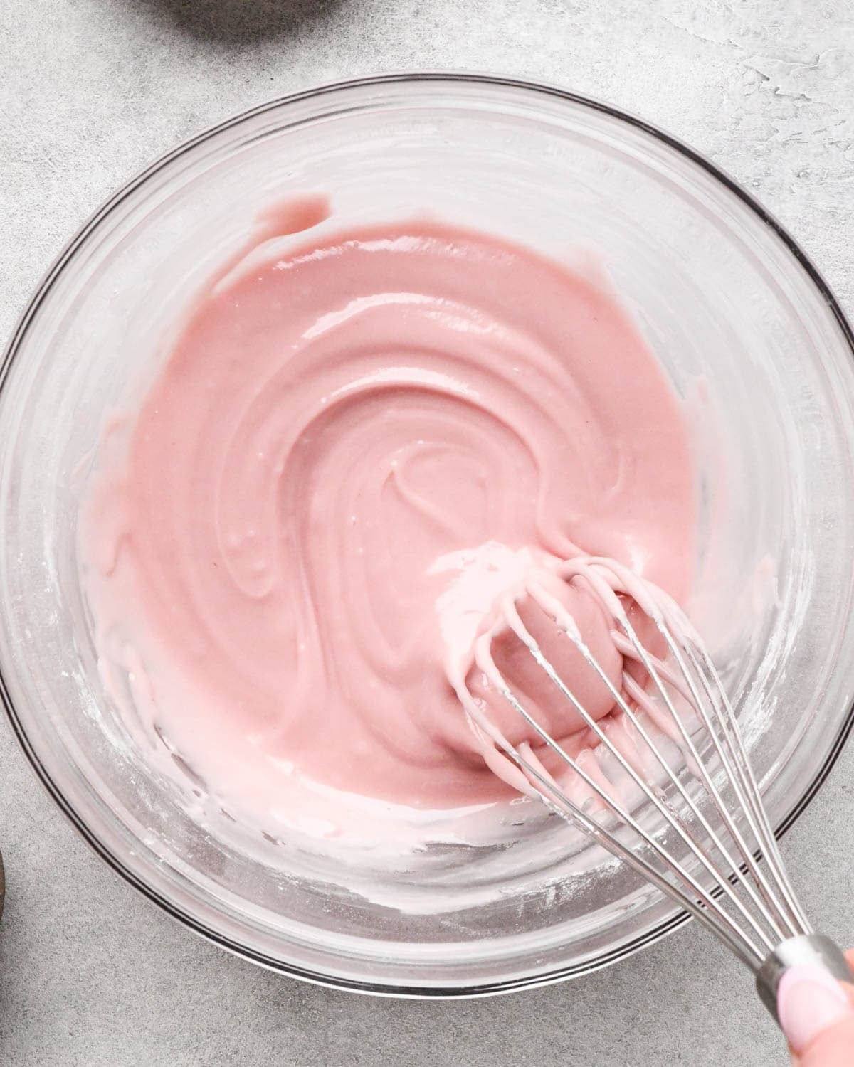 making icing for homemade pop tarts - strawberry icing being whisked together in glass bowl with a wire whisk