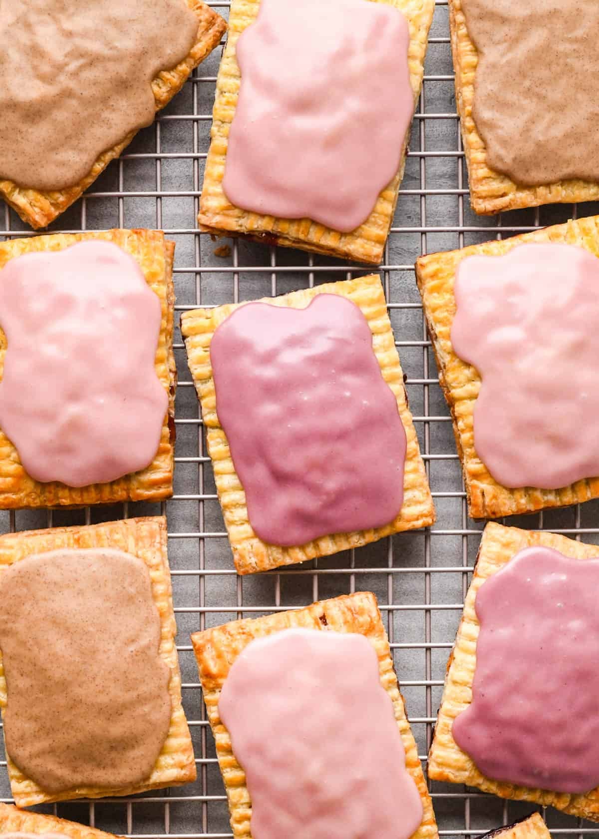 9 homemade pop tarts with icing on top on a wire metal cooling rack, 3 strawberry, 3 blackberry and 3 cinnamon brown sugar pop tarts