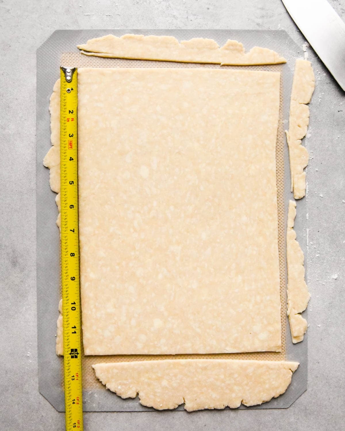 making homemade pop tarts - a rectangle of dough rolled out, the long side is being measured with a tape measure and trimmed