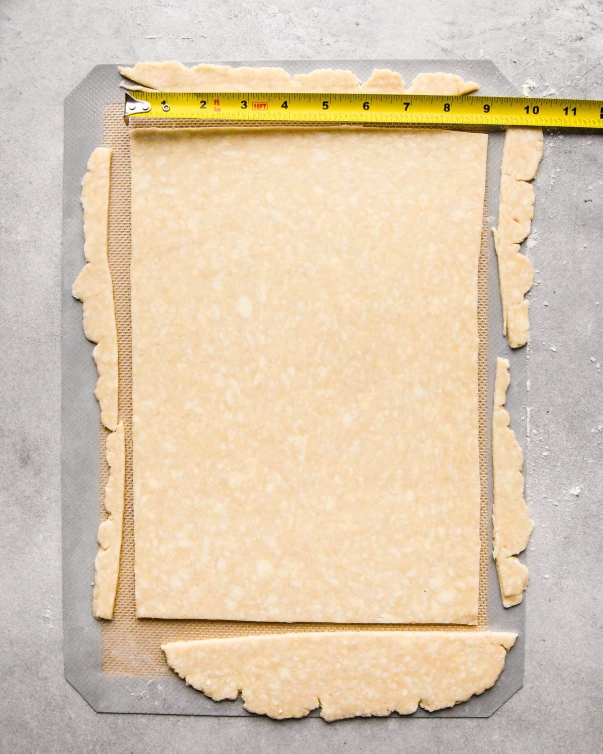 making homemade pop tarts - a rectangle of dough rolled out, the short side is being measured with a tape measure and trimmed