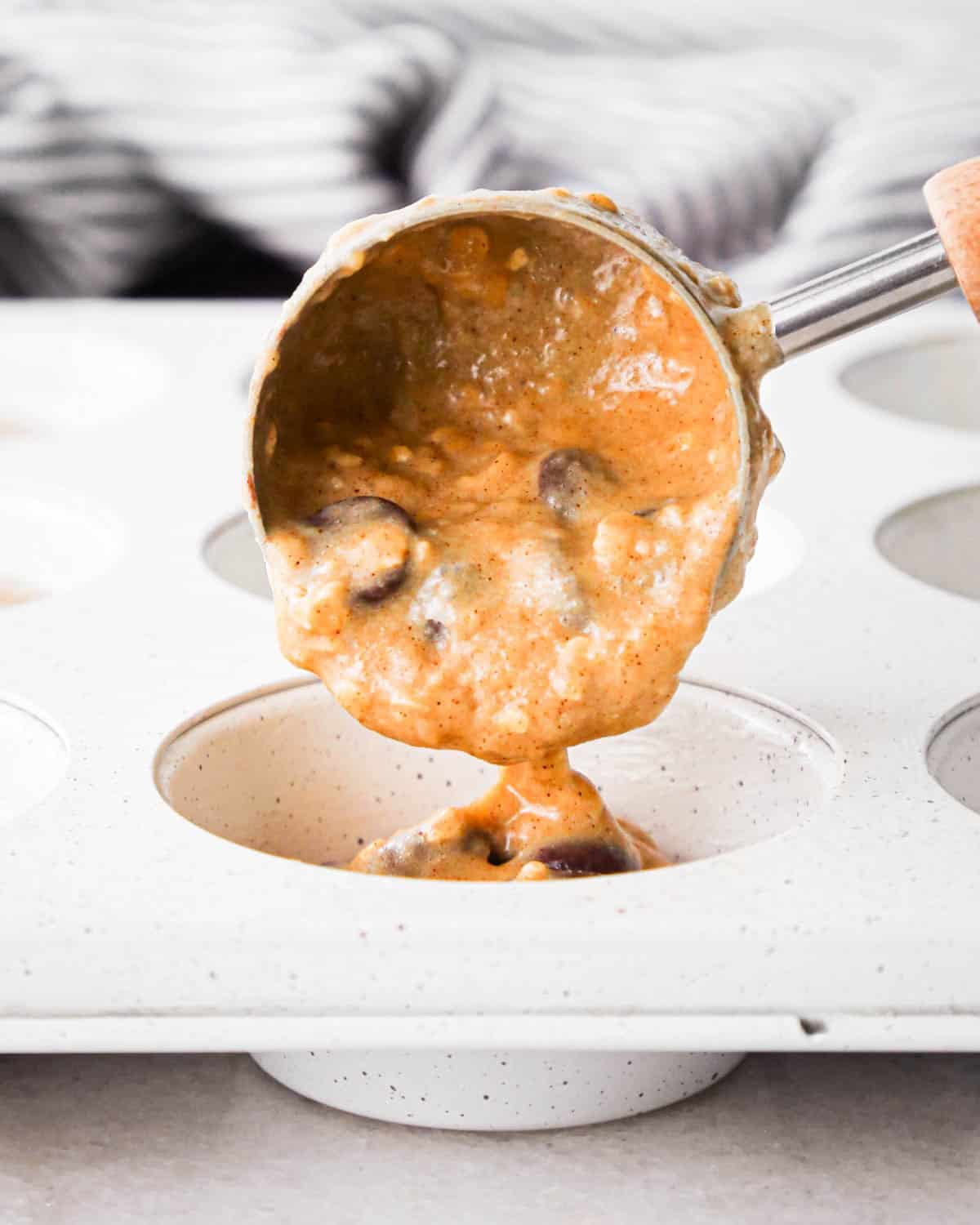 making oatmeal chocolate chip muffins - a cookie scoop putting batter into the well of a muff pan