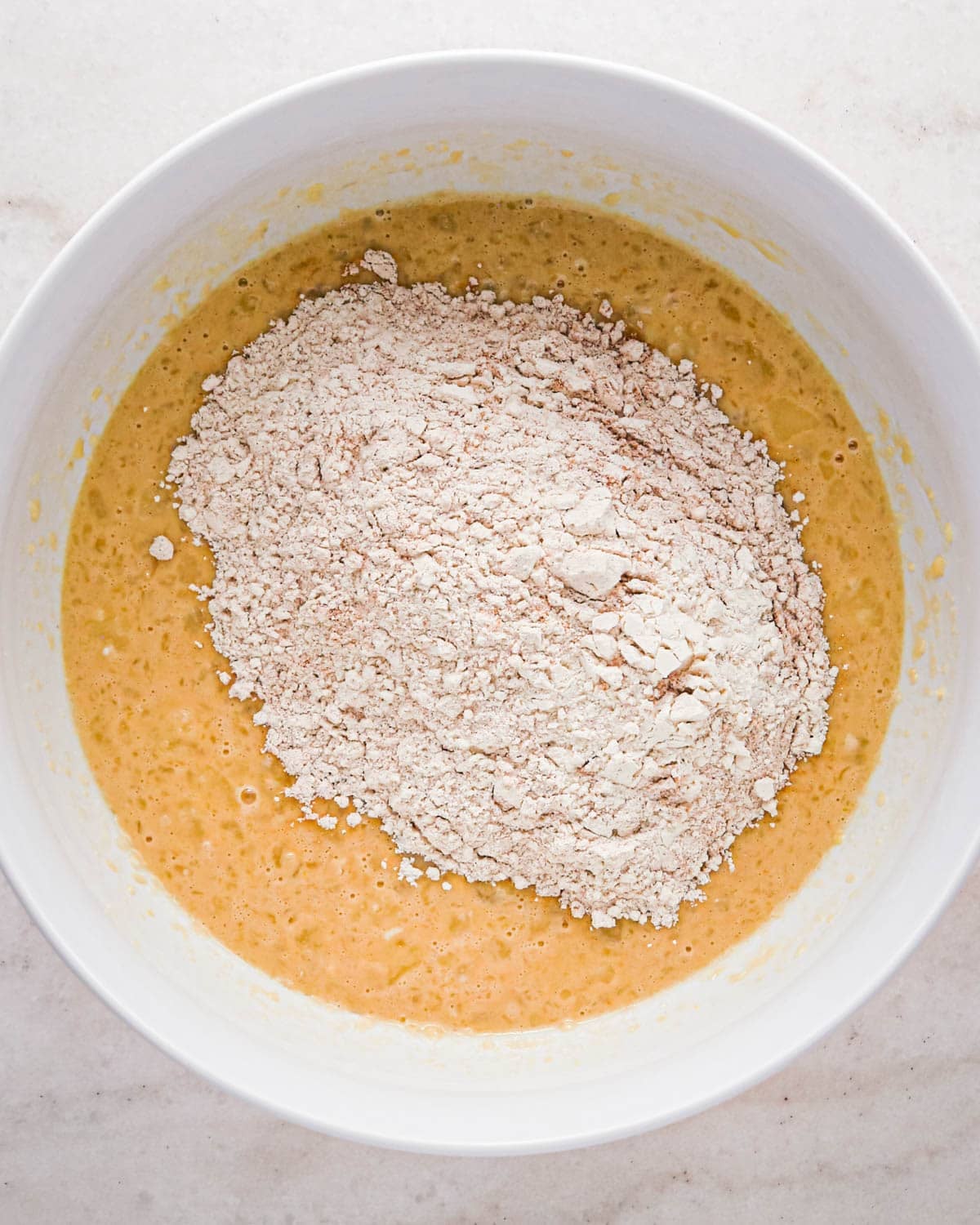 making oatmeal chocolate chip muffins - dry ingredients added to the wet ingredients in a white bowl before mixing