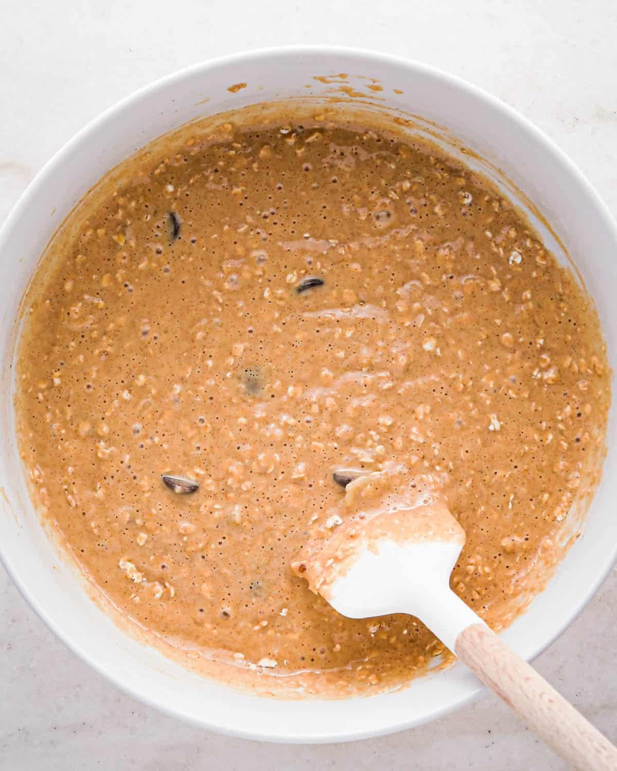 making oatmeal chocolate chip muffins - final batter in a white bowl with a white and wood spatula