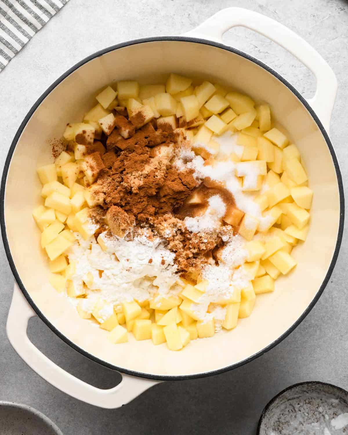 making apple hand pies filling - diced and peeled apples, cinnamon, brown sugar, granulated sugar, cornstarch, vanilla and nutmeg in a white pot before cooking