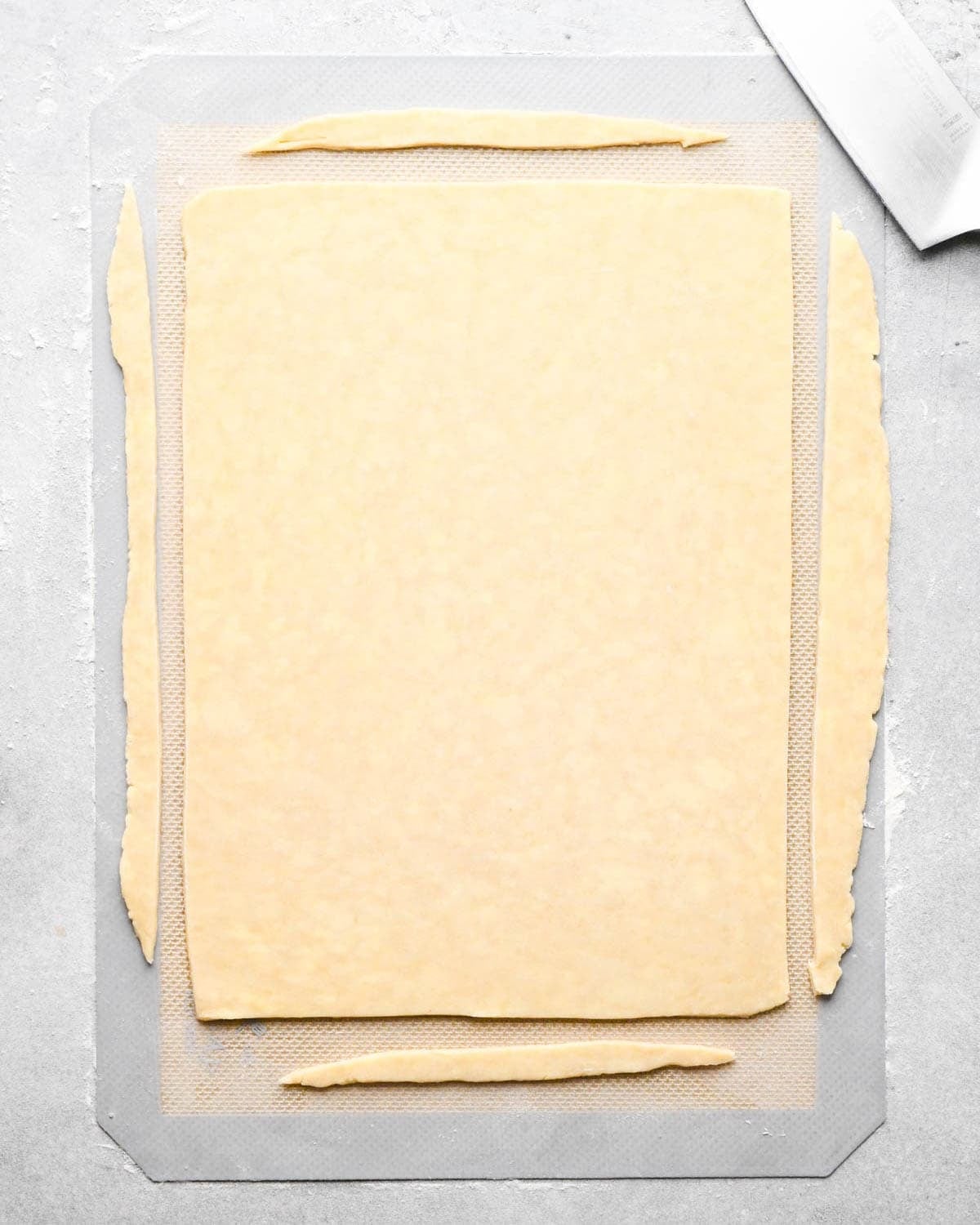 making apple hand pies crust - dough rolled into a large rectangle on a floured silicone baking mat with the edges trimmed off to make them straight