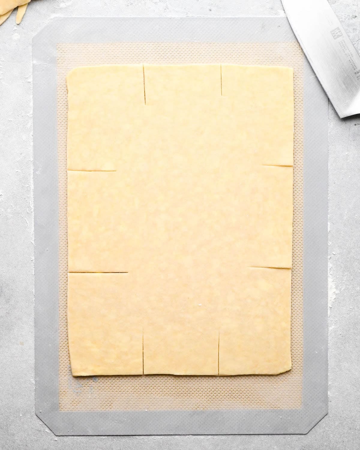 making apple hand pies crust - dough rolled into a large rectangle on a floured silicone baking mat with each of the sides scored twice.