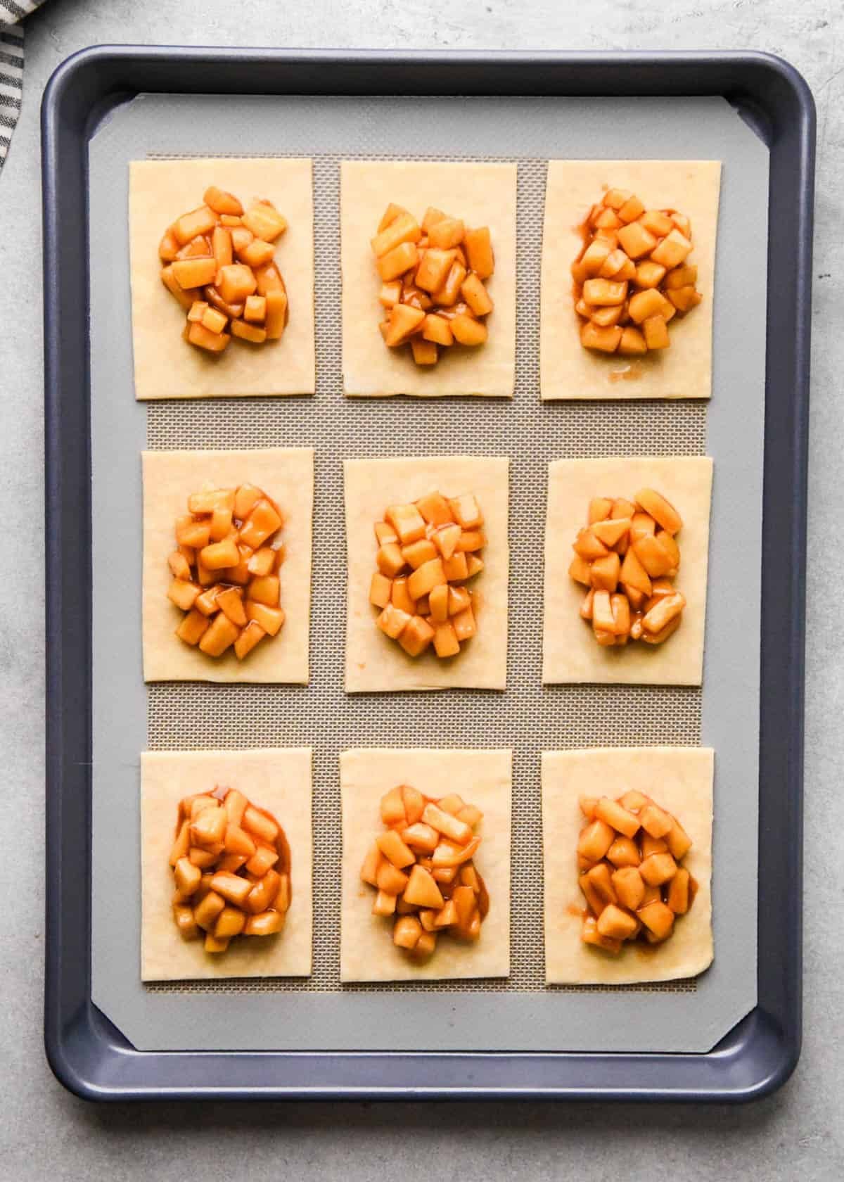 assembling apple hand pies - 9 hand pies filled with apple filling on a baking sheet lined with parchment paper without the top crust on