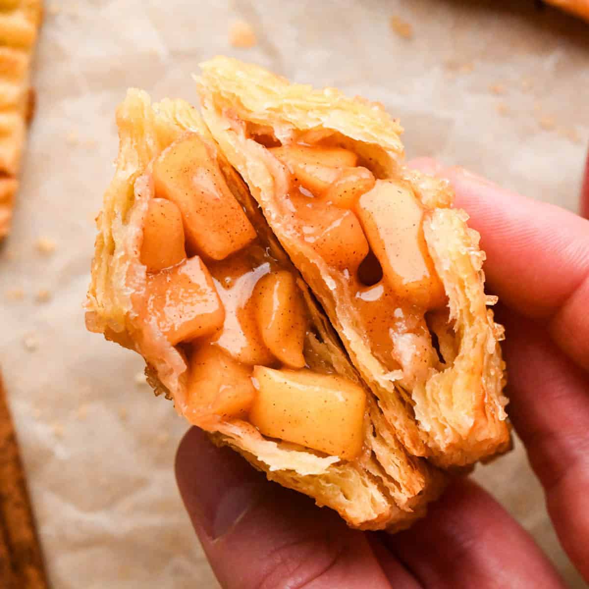 a hand holding two halves of an apple hand pie so the gooey cinnamon apple filling is showing