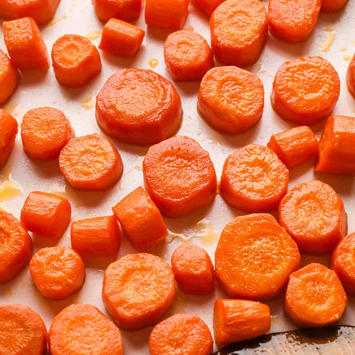 perfectly golden maple glazed carrots on a white baking sheet with a wooden spatula in the bottom right corner
