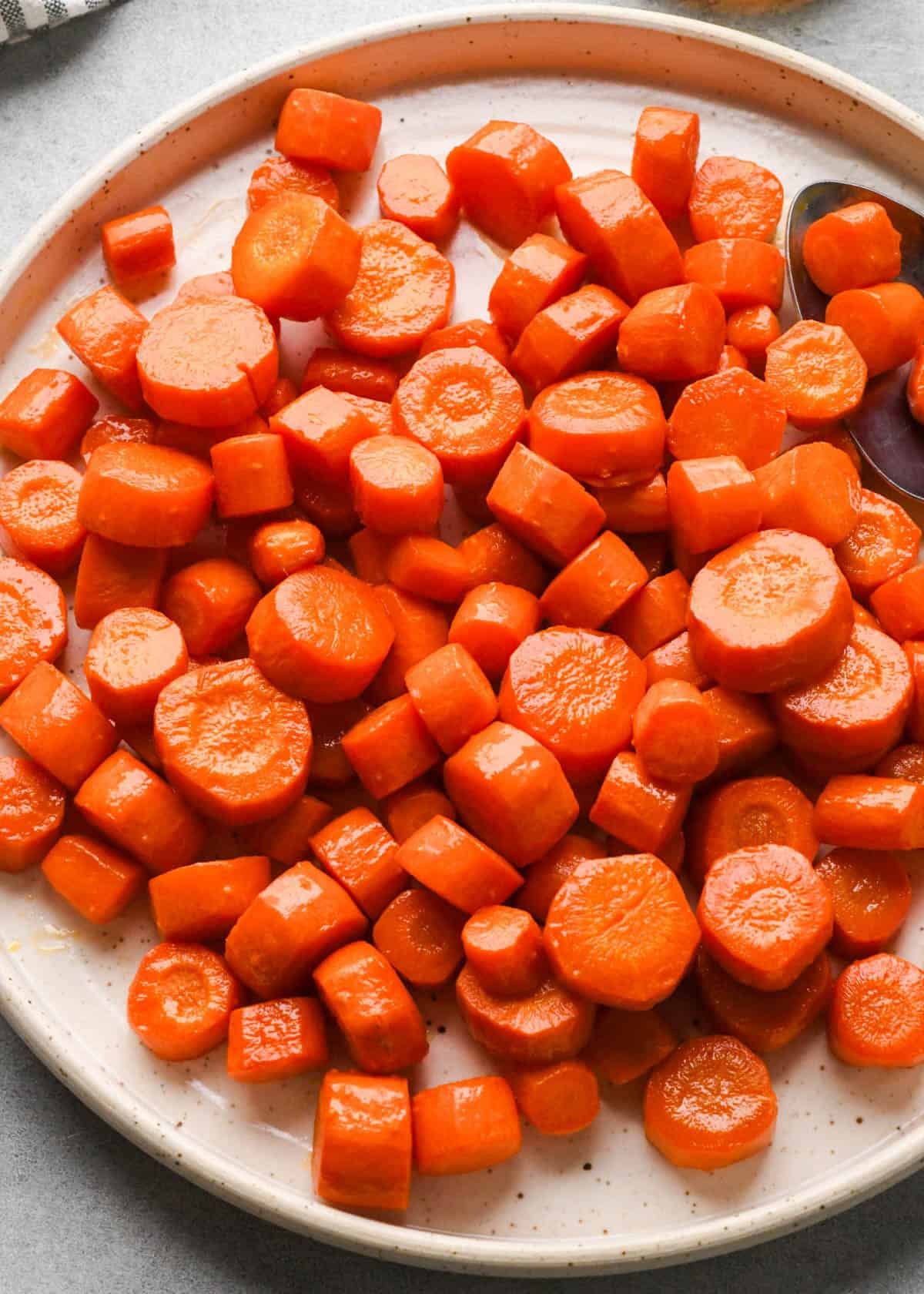 maple glaze carrots on a white plate with a white spoon in the top right corner