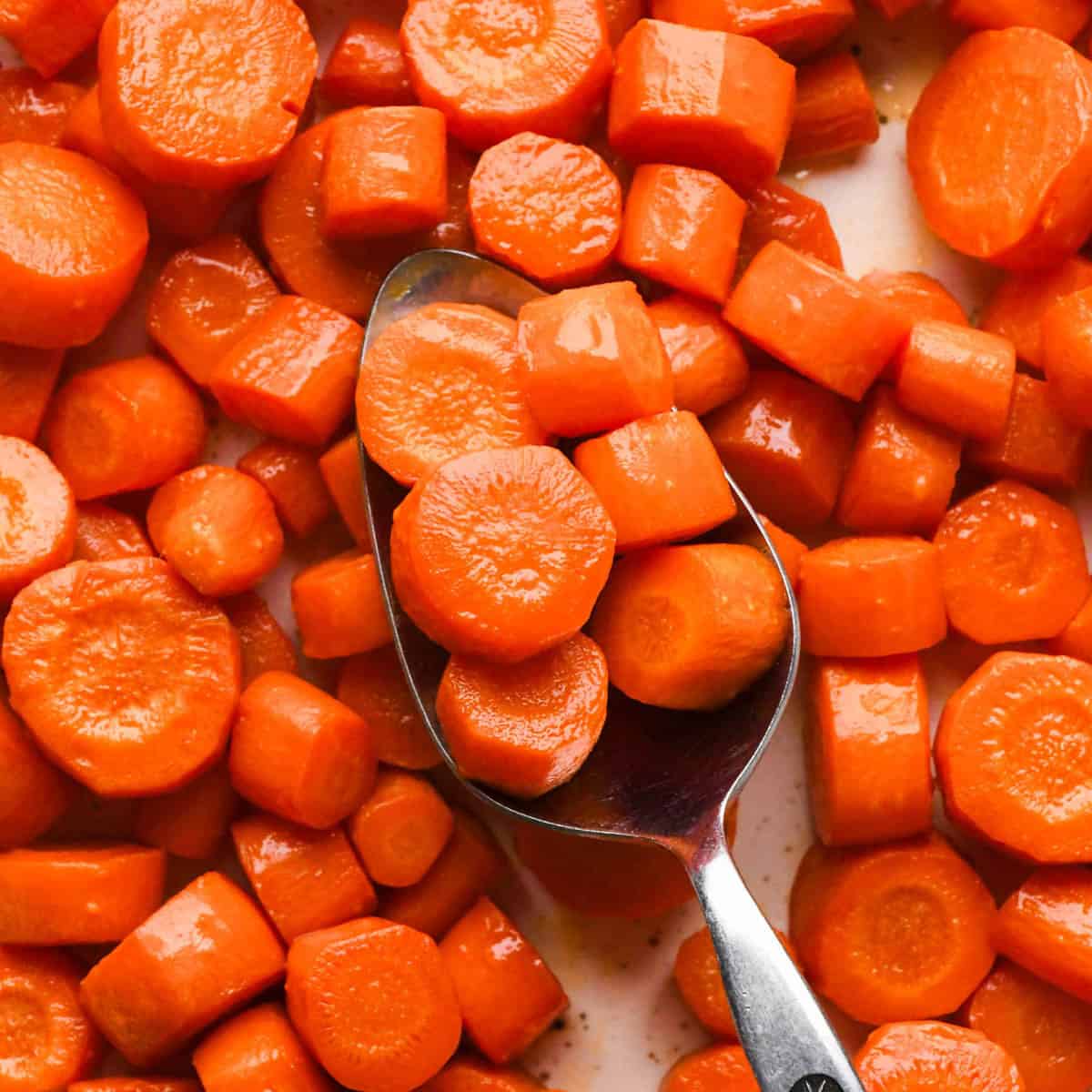 maple glazed carrots on a white plate with a silver spoon taking a scoop of carrots from the middle of the plate