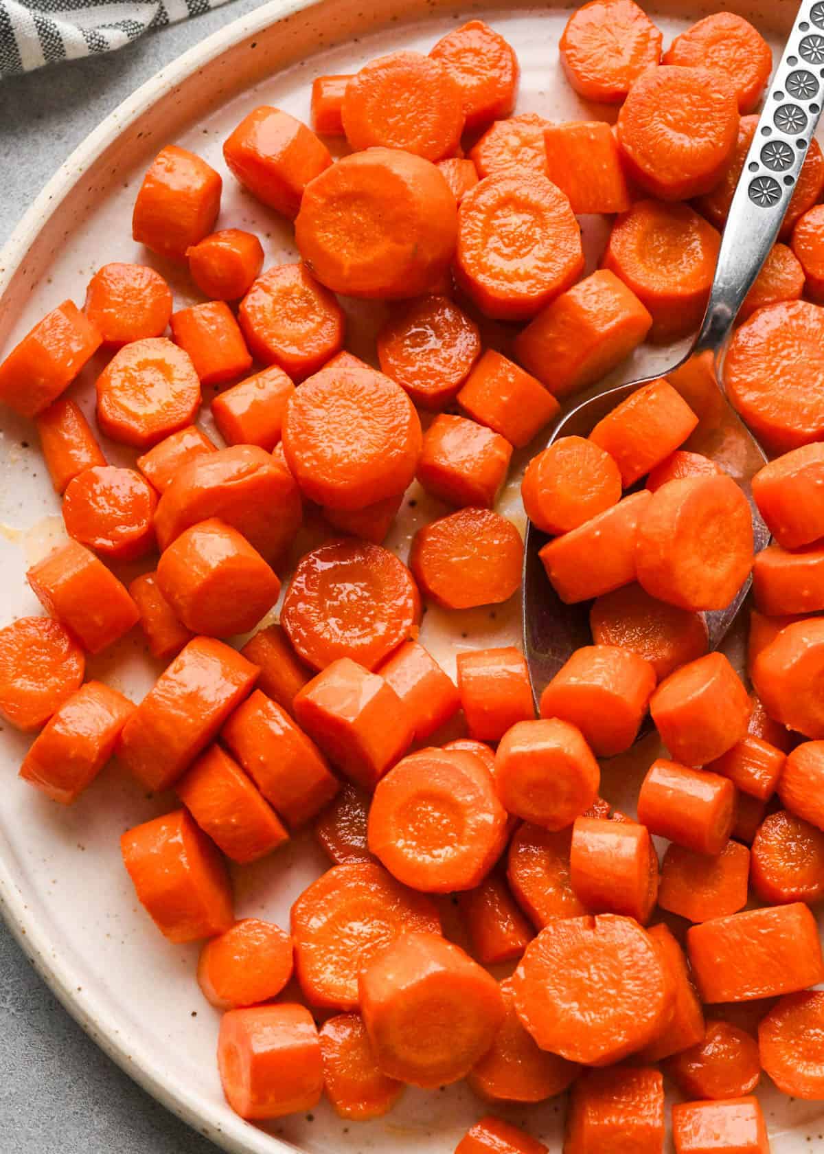 maple glazed carrots on a white plate with a silver spoon taking a scoop of carrots