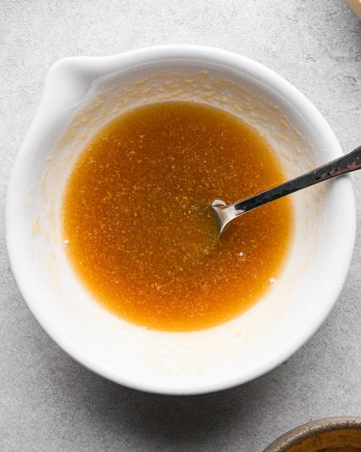 making glazed maple carrots - melted butter and maple syrup in a white bowl with a silver spoon